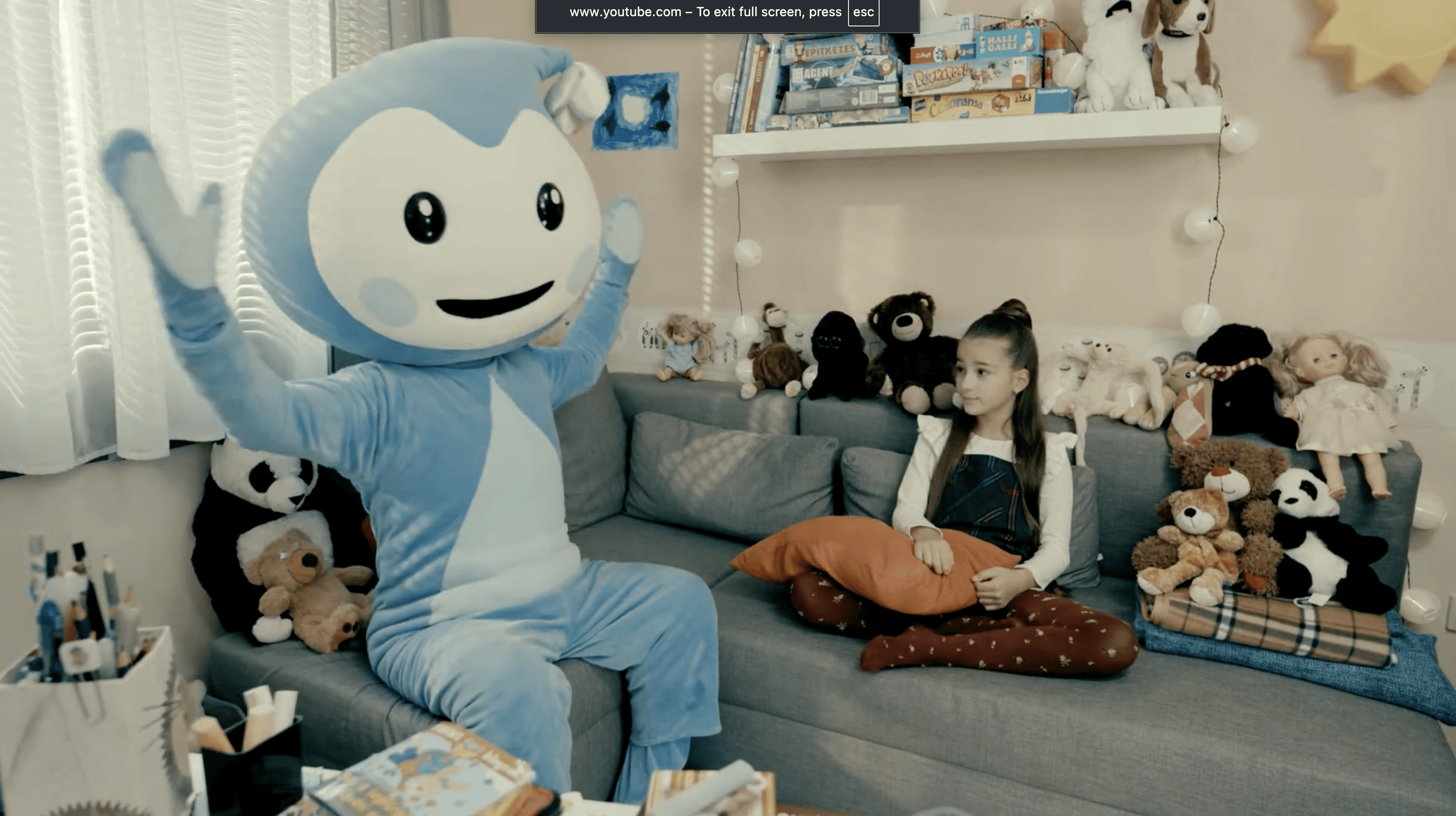 Cseppbarát kék kabalafigurája kitárt kezekkel énekel a kislánynak aki szomorú.