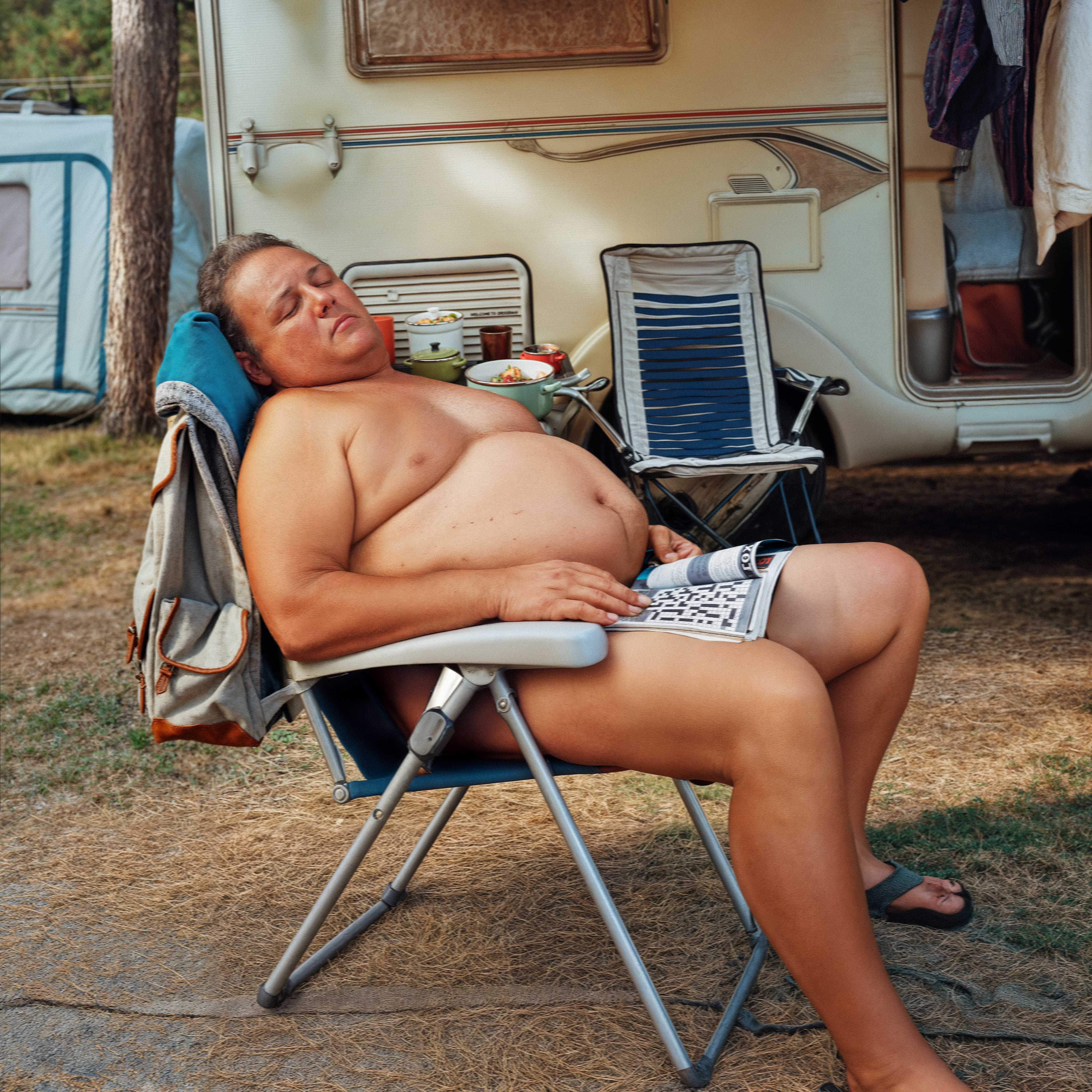 a nude man taking a nap on a lawn chair outside