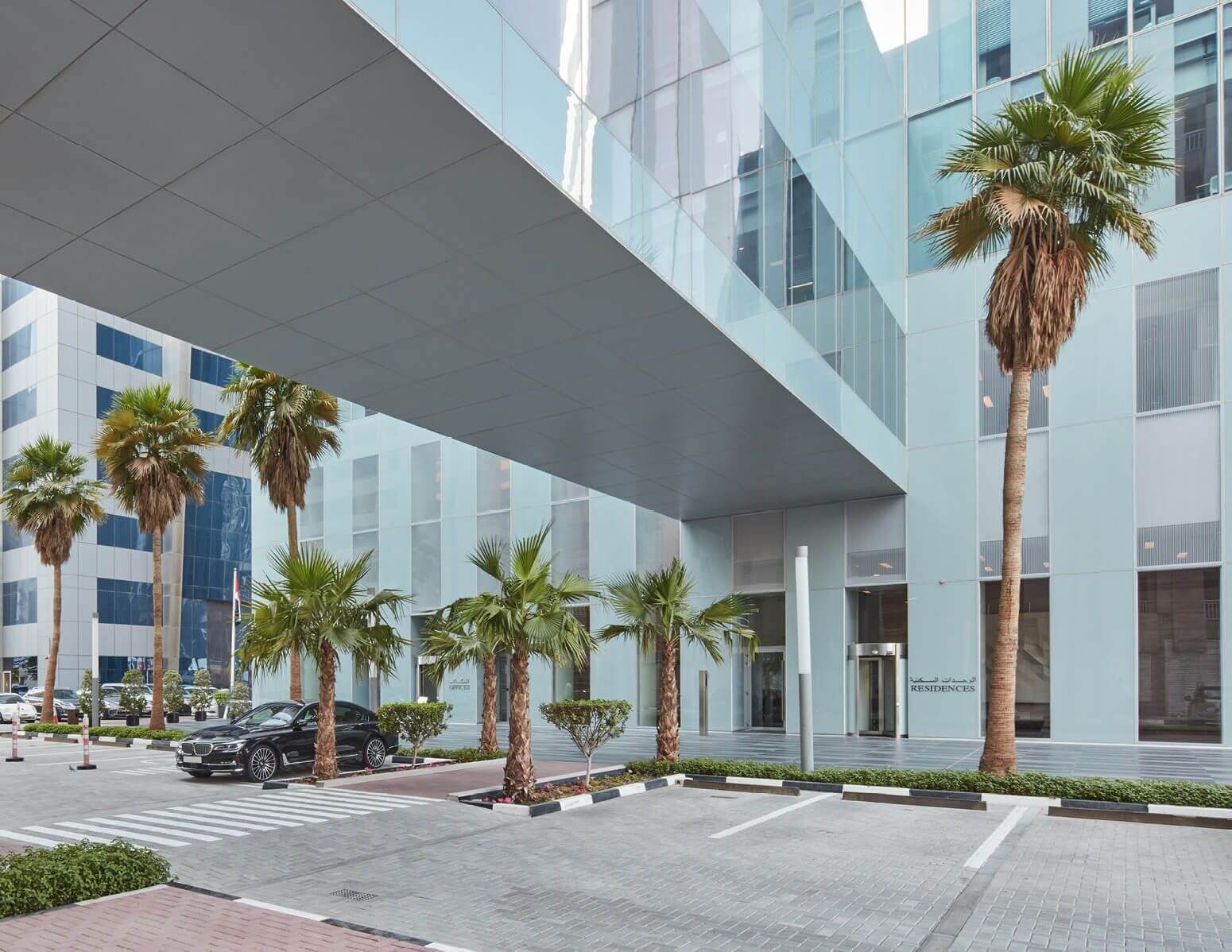 Elegant entrance to Rolex Tower Residences with palm trees, offering a sophisticated real estate experience.
