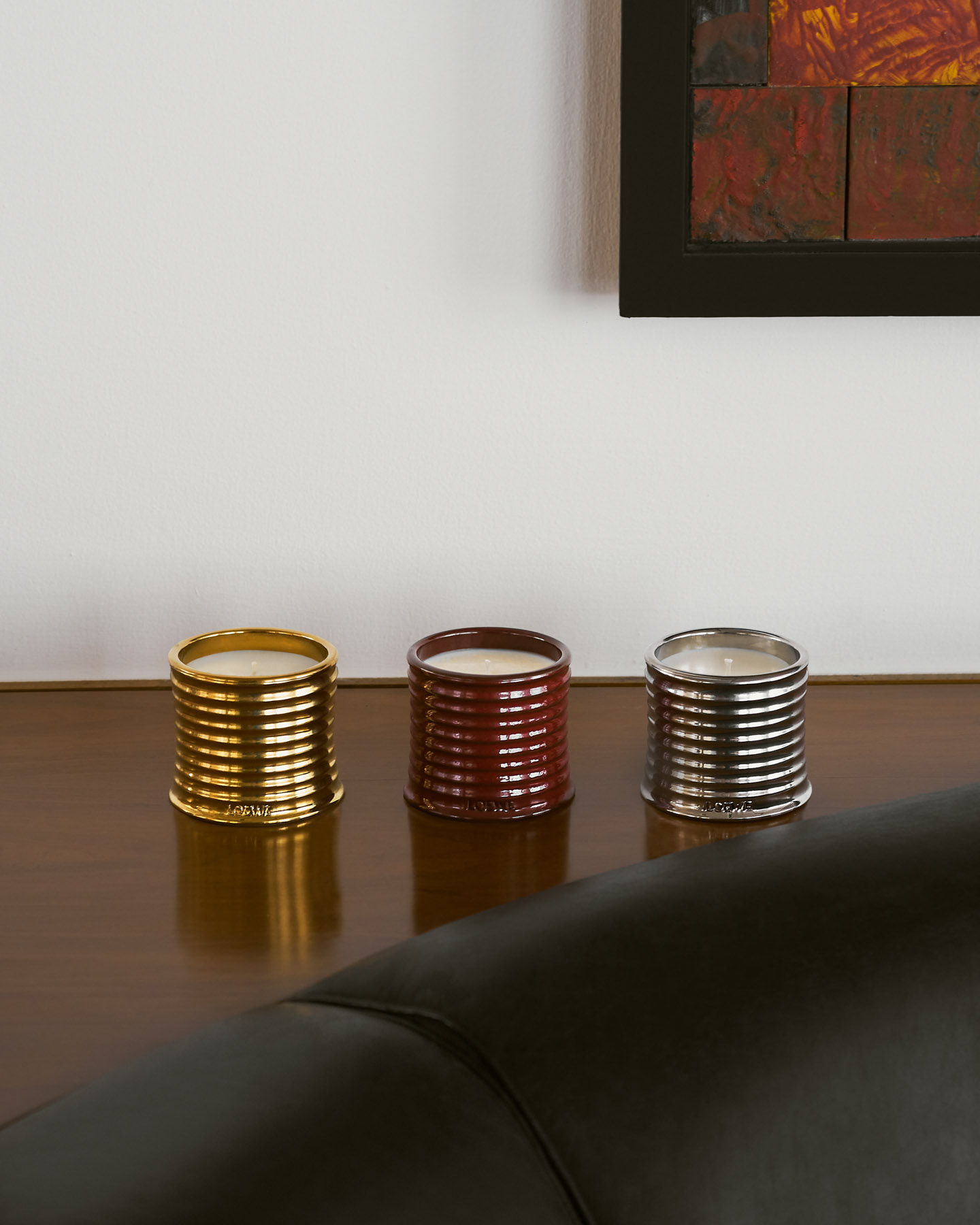 The LOEWE Home Scents candle collection in gold, red and silver finishes displayed on a walnut table within Estudio Lamela.