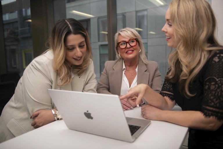 Two professional women, one wearing glasses, looking at a laptop together in an office setting