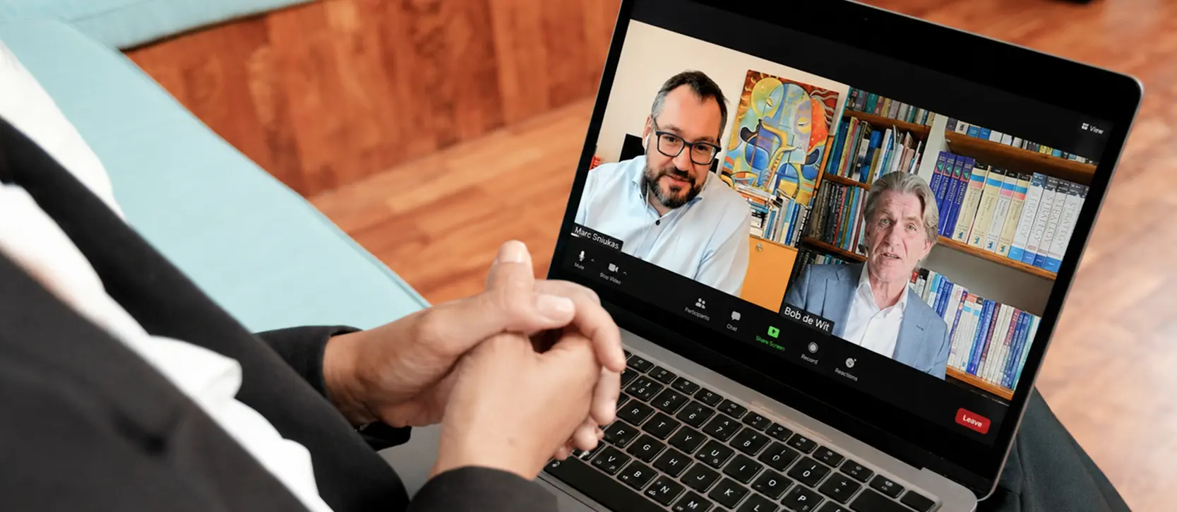 Student watching a live online session with instructors Marc Sniukas and Bob de Wit on a laptop.