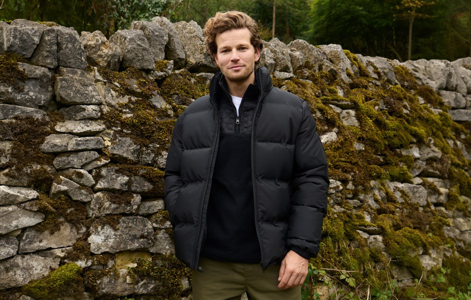 Young man wearing modern clothes walking past a dry stone wall in the countryside