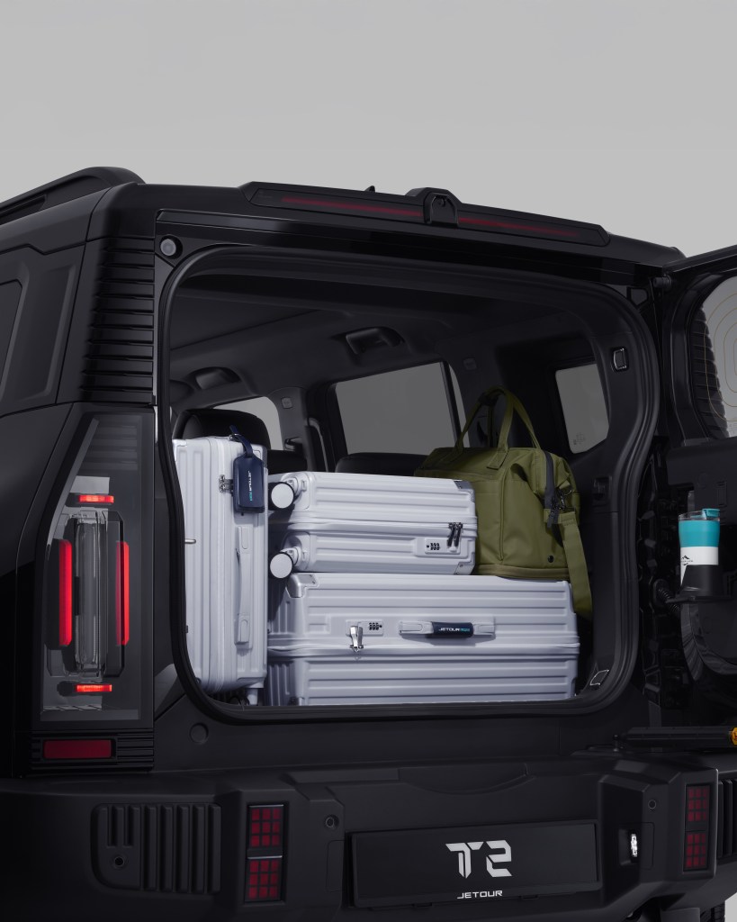 The interior of a black SUV's trunk loaded with white suitcases and a green duffel bag, featuring rear lights and a travel mug.
