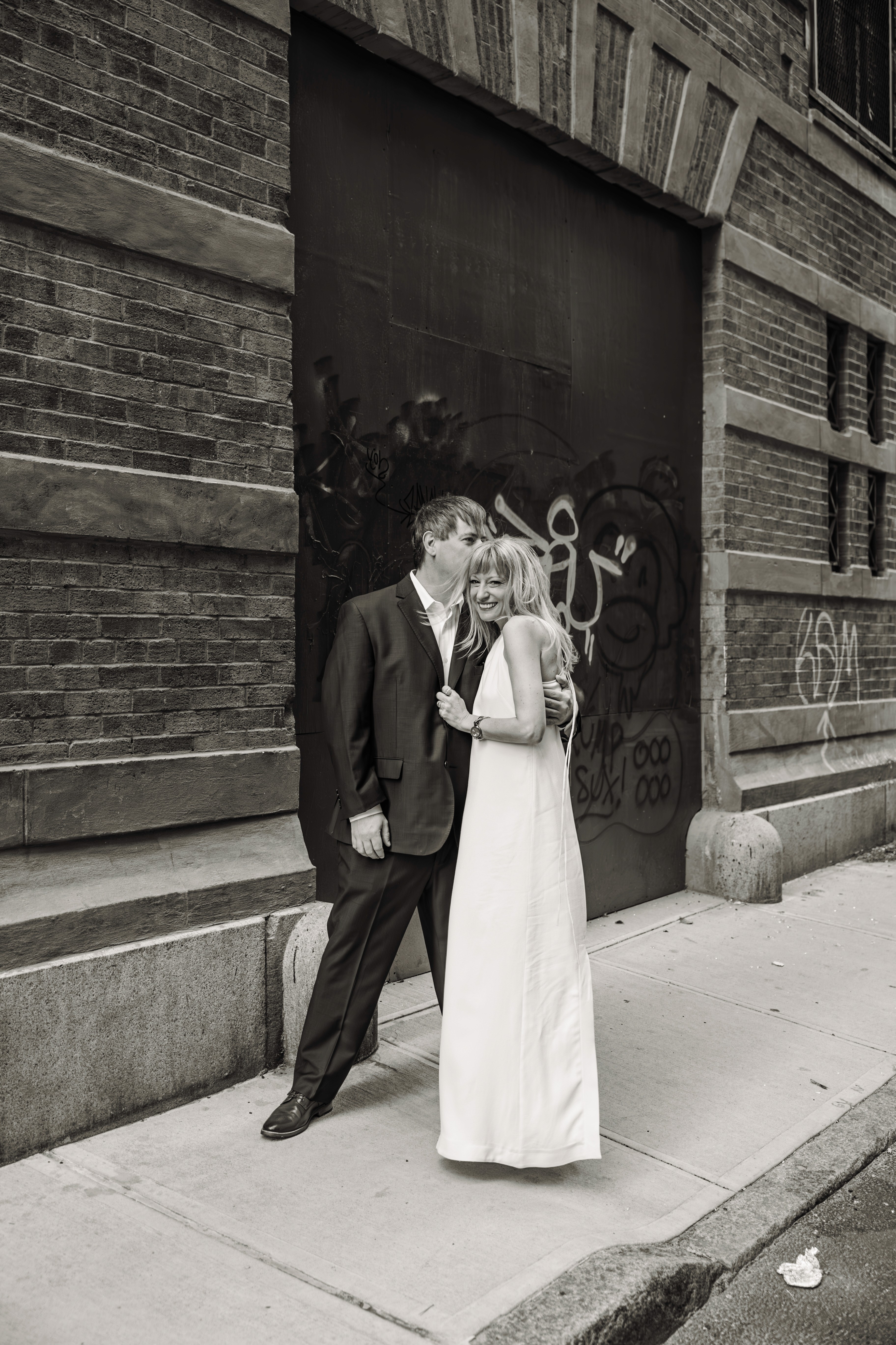 She's leaning in close, whispering in his ear beneath the iconic Staple Street Bridge in downtown Tribeca, NYC — intimate, romantic couples photography by Lizz Spano Photography, New York City couples photographer.