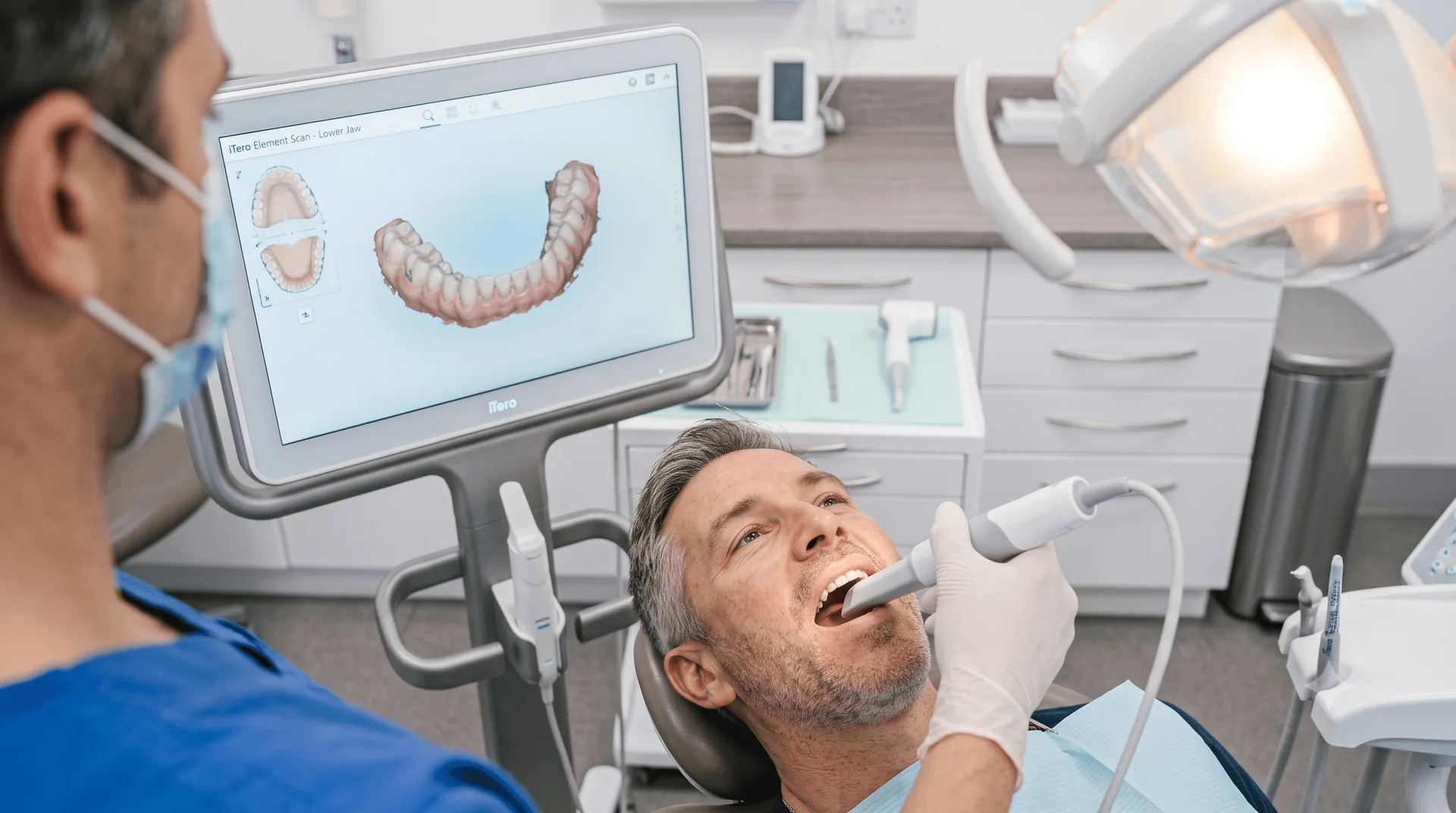 Dentist treating a smiling patient, with a digital scan of teeth on the monitor
