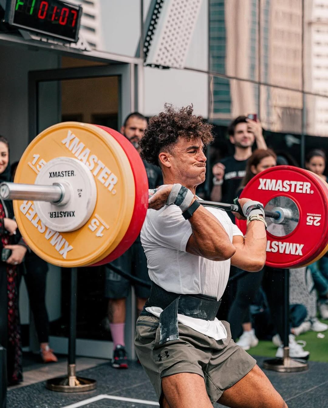 A shirtless man intensely using battle ropes in a gym, with another man in the background.