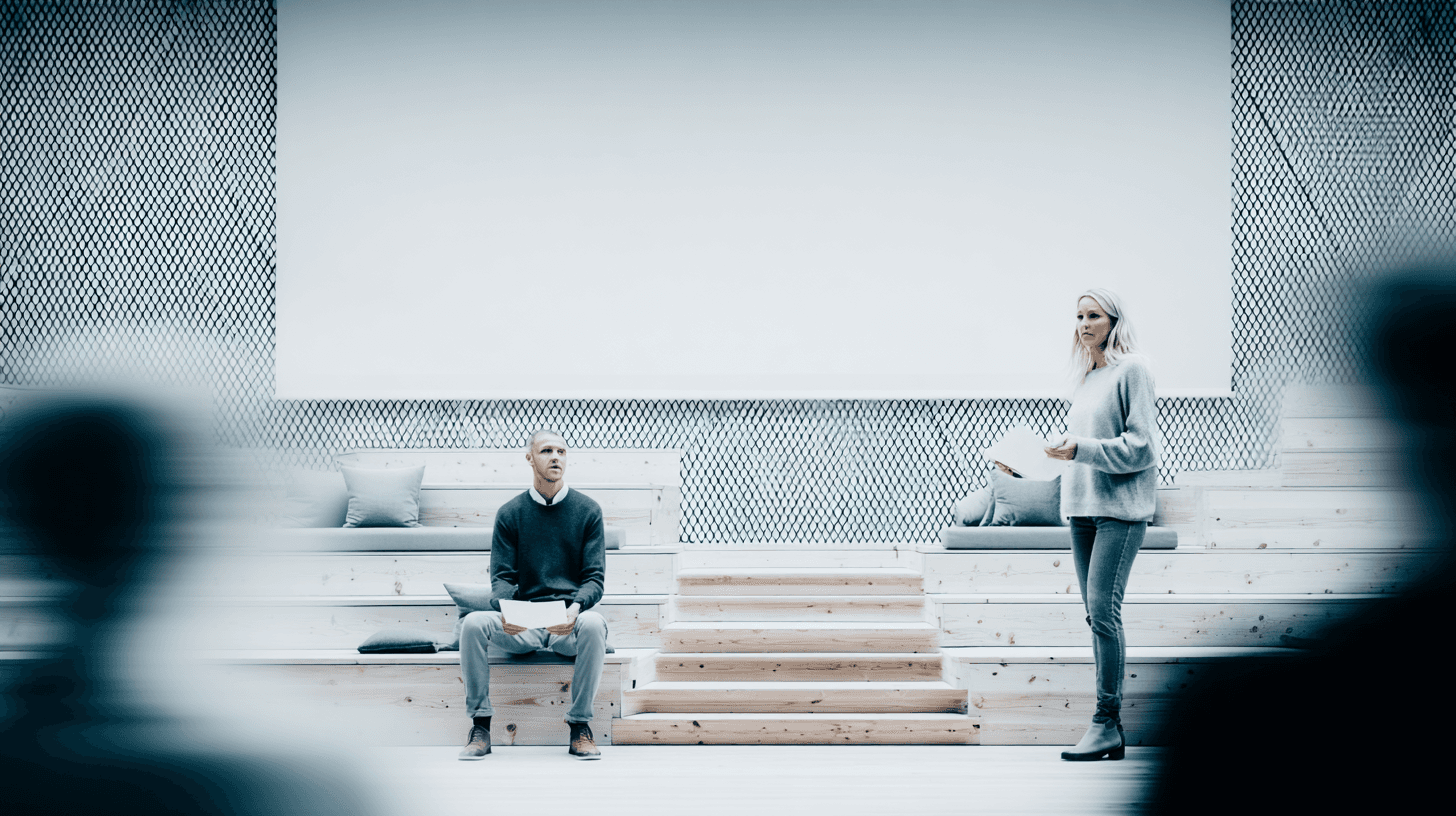 A smiling young man with crossed arms, wearing a plaid shirt and white t-shirt, poses against a dark background.