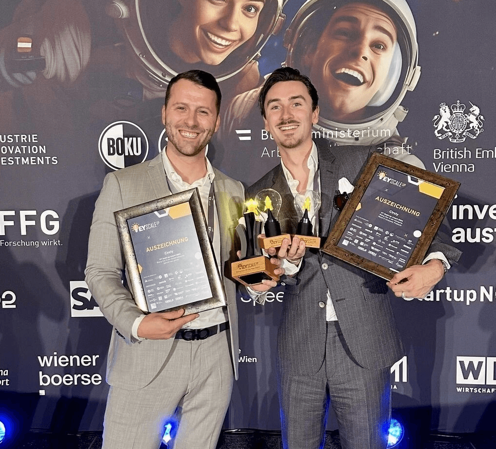 Eric Weisz und Benedikt Marsen (Circly) halten Auszeichnungen und Trophäen bei einer Preisverleihung vor einer Sponsoren-Fotowand.