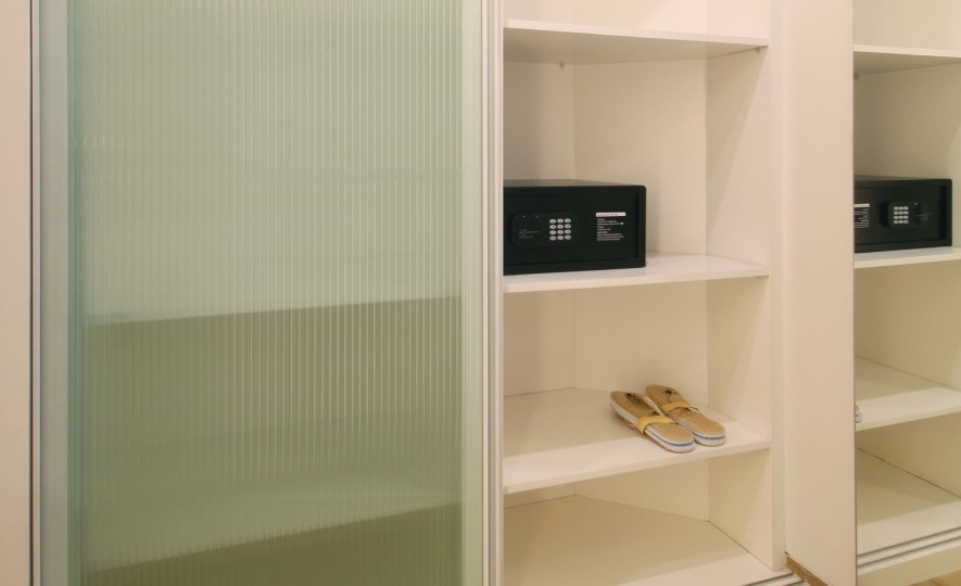 Bedroom Closet Detail: Close-up of the open wardrobe shelves showing the in-room safety deposit box and complimentary slippers provided at Echo Beach Suite, Bali.