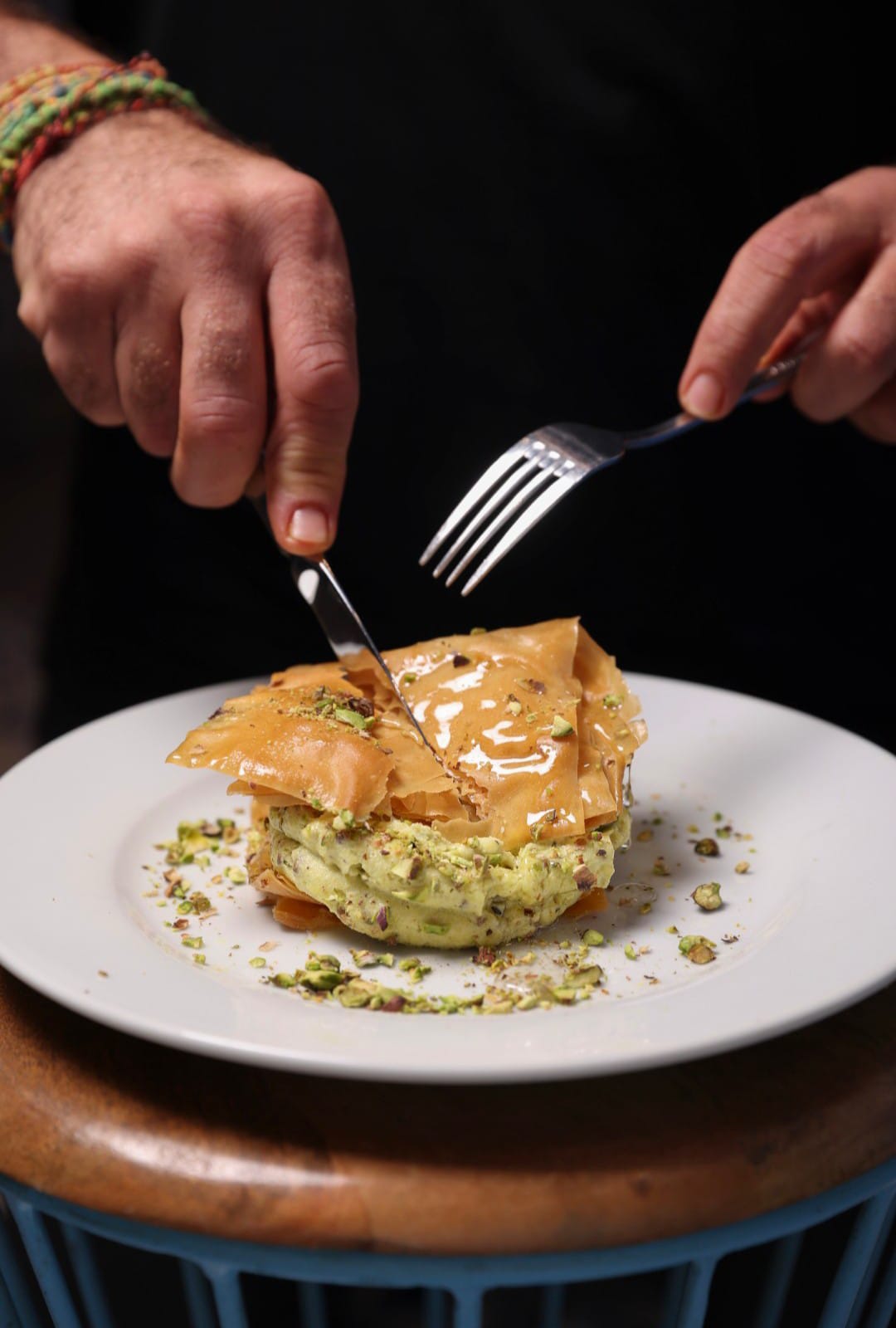 White plate with roasted carrots served on green sauce, topped with almonds and fresh herbs, held by a hand over a dark table.
