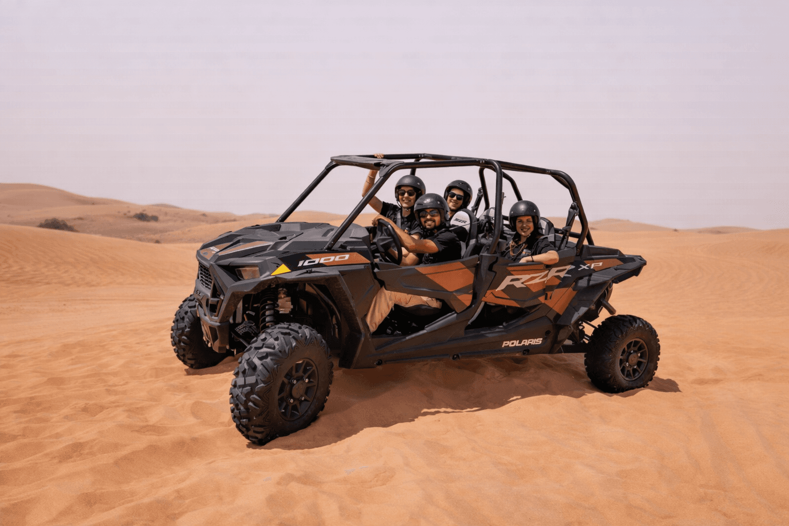 A group of four friends enjoying a desert safari in a black and orange Polaris RZR 1000cc 4-seater buggy with Dune Quest Tours