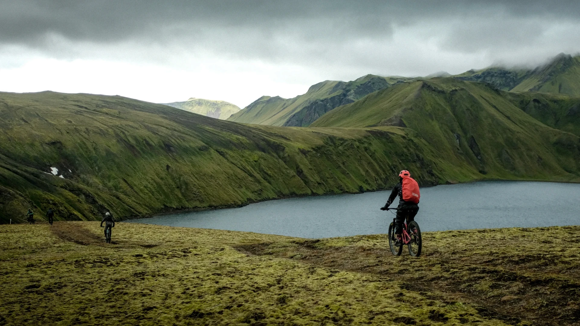 Two men ride away from camera by a lake in the highlands of Iceland