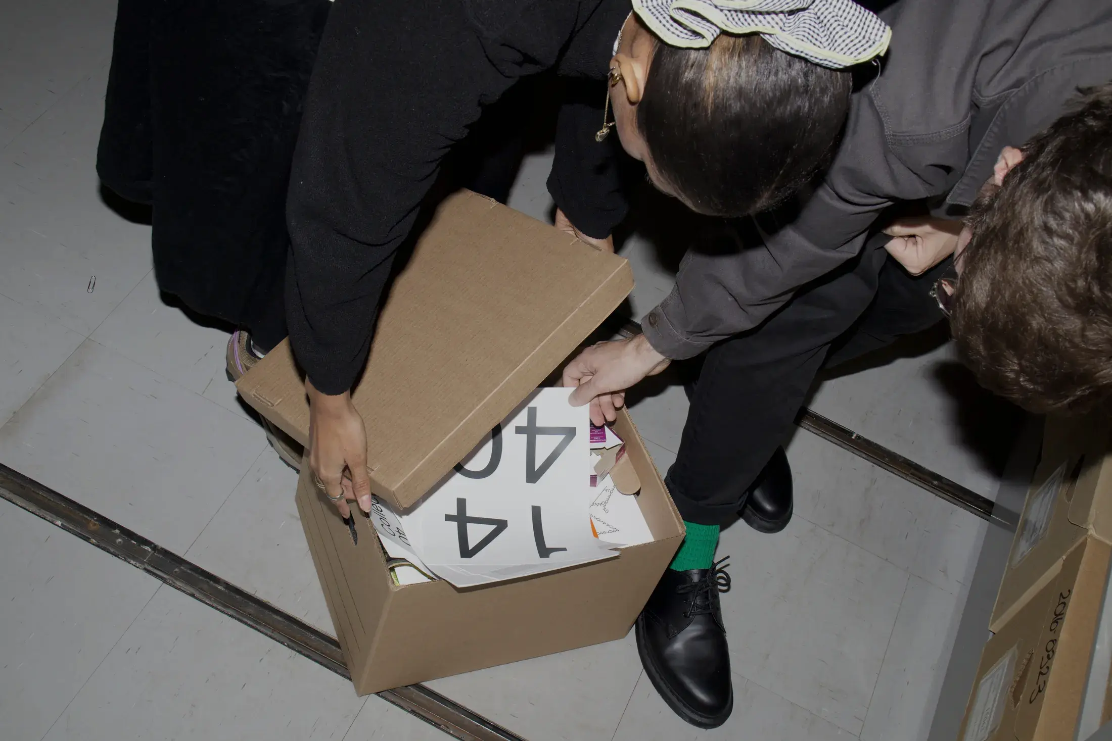 Deux personnes ouvrant une boîte d’archives en carton contenant des imprimés typographiques du Collectif1440, vue du dessus.