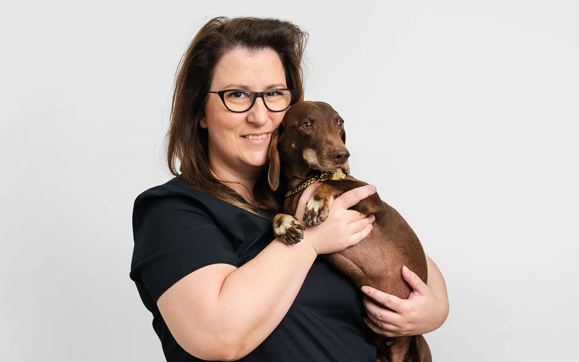 Dr. Lidija Krvavac holds a calm brown dachshund at Noble Veterinary Clinic, gently supporting the dog during a consultation.