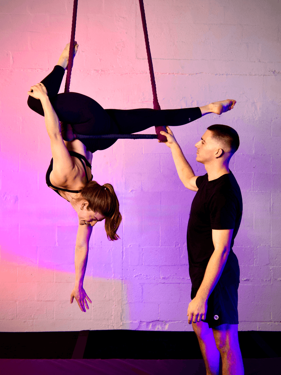 a young girl on a trapeze assisted by a male coach