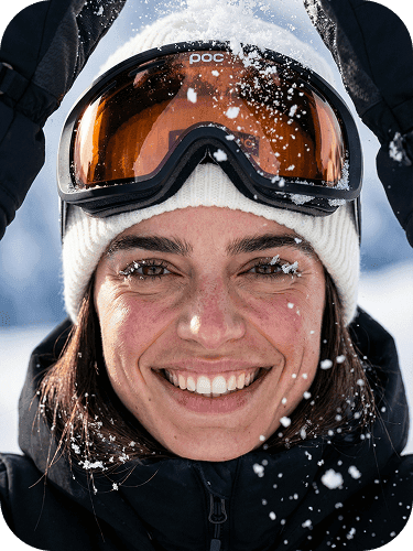 Smiling woman wearing ski goggles, fresh snow falling in an alpine setting