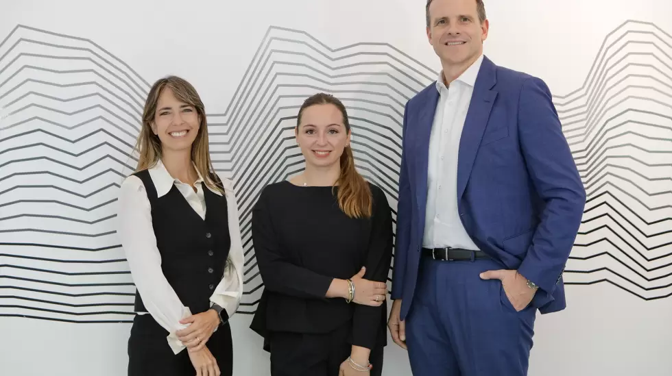Three founders smile at the camera in front of a wavy, black and white line background.