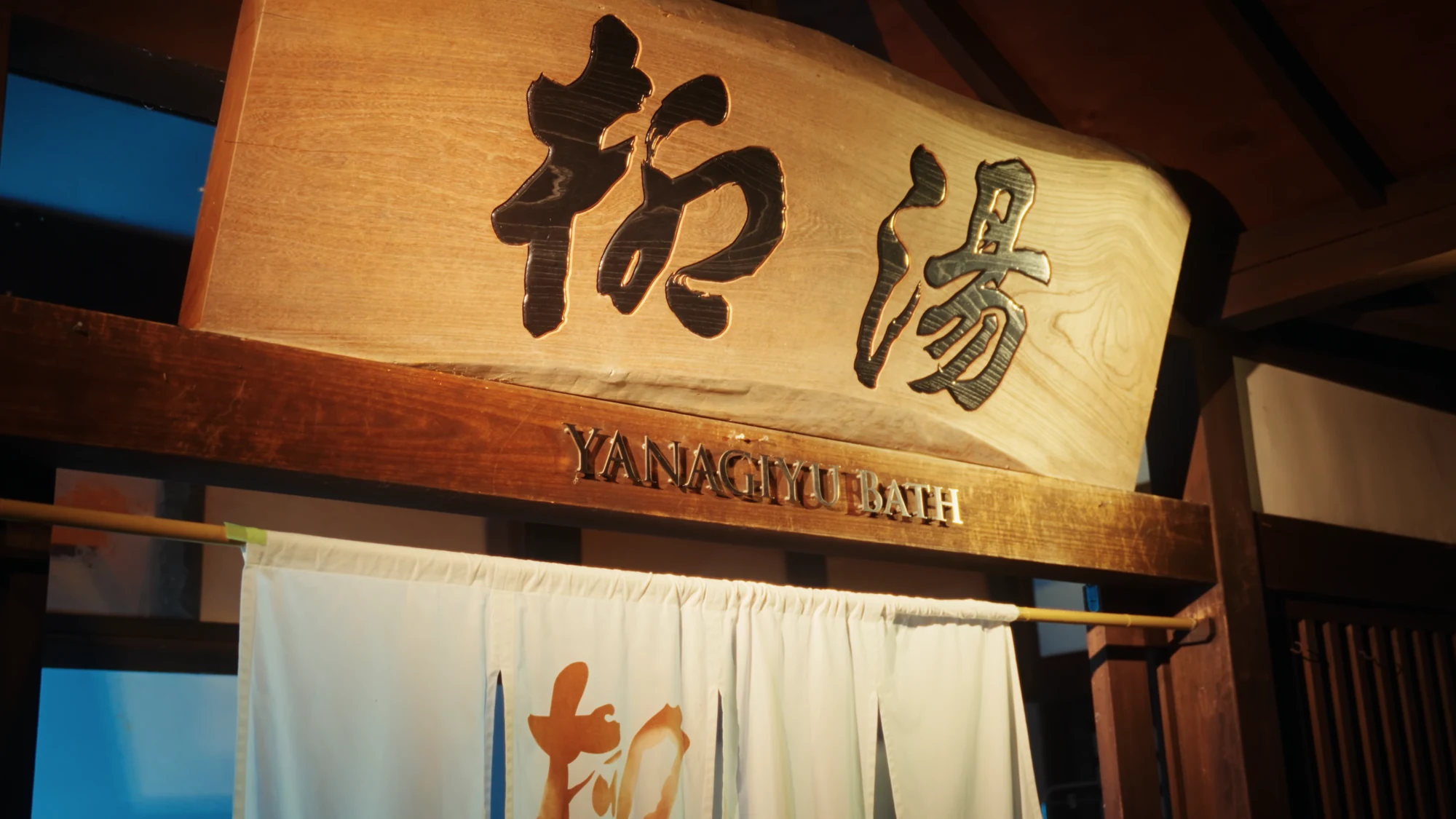The carved name board of Yanagi-yu bathhouse in Kinosaki above its hanging noren.