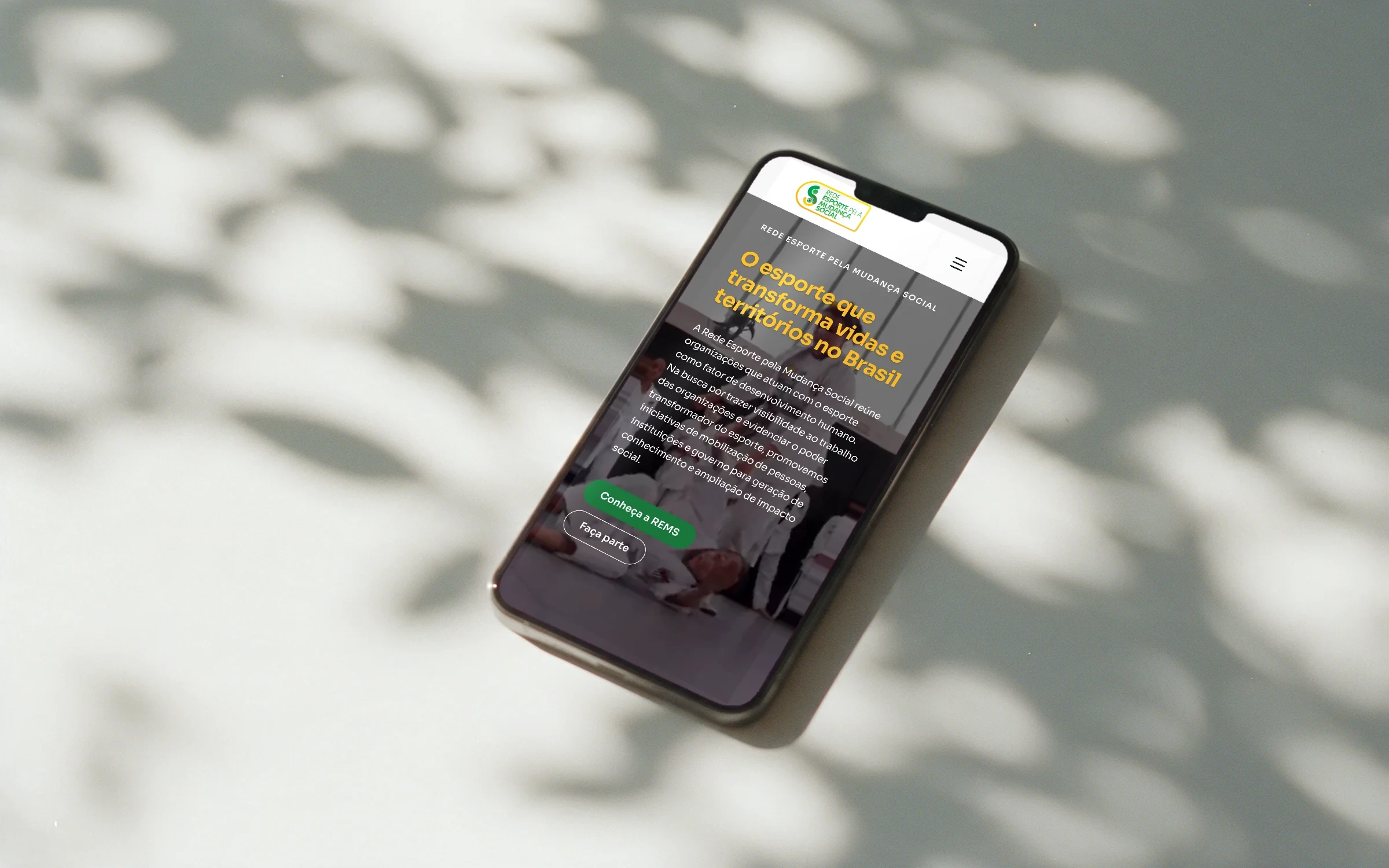 Página inicial do site da REMS num celular sobre a mesa