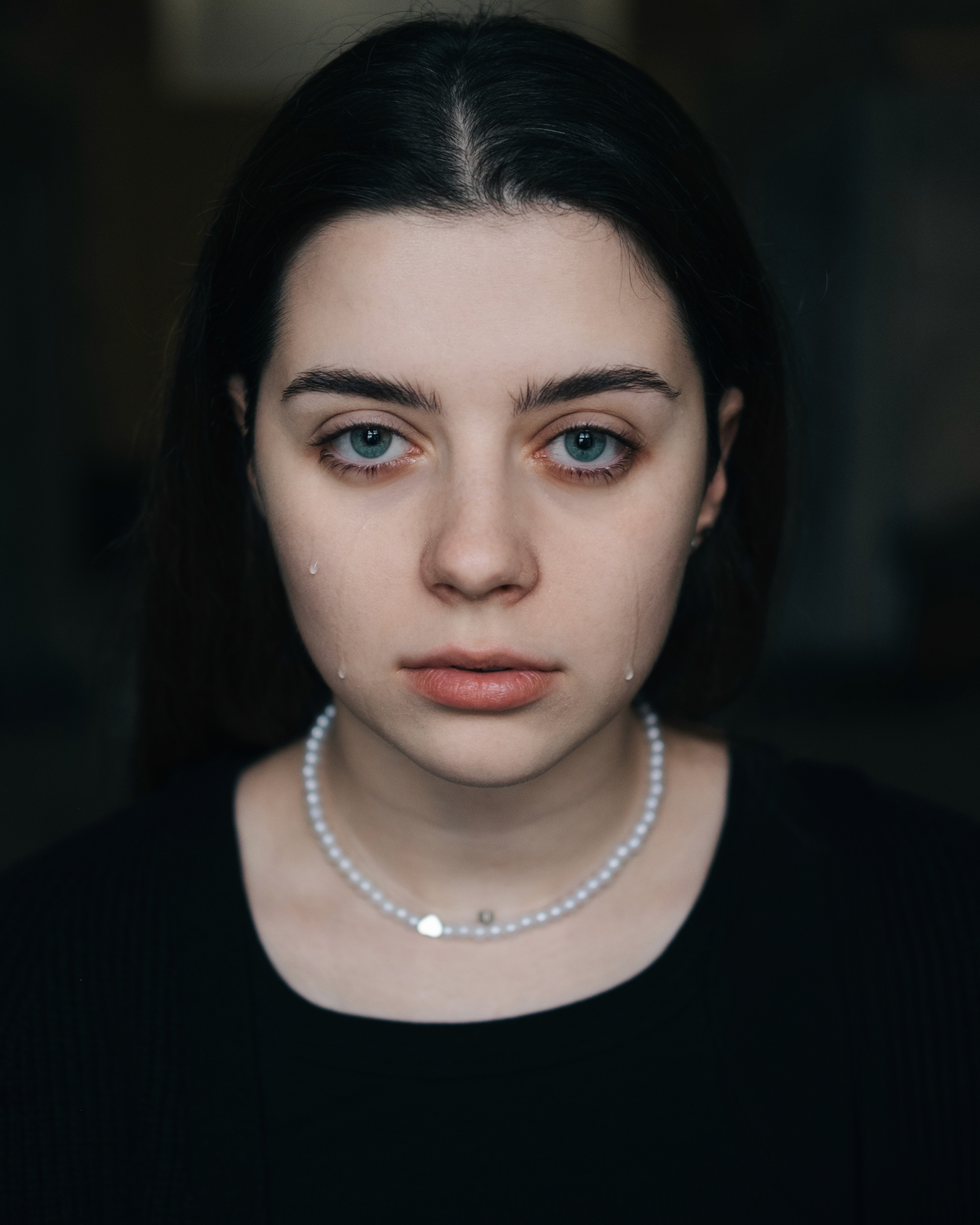 Minimal close-up of a person with tears on their cheeks, looking directly at the camera.
