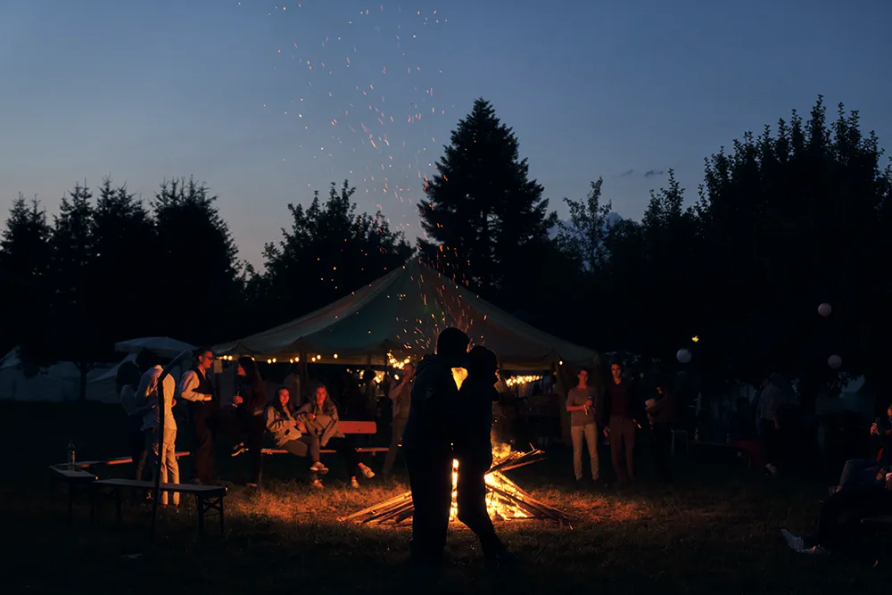 Küssendes Brautpaar als Silhouette vor einem Lagerfeuer bei einer Outdoor-Hochzeit in der Abenddämmerung, Hochzeitsfotografie Eva Sitko