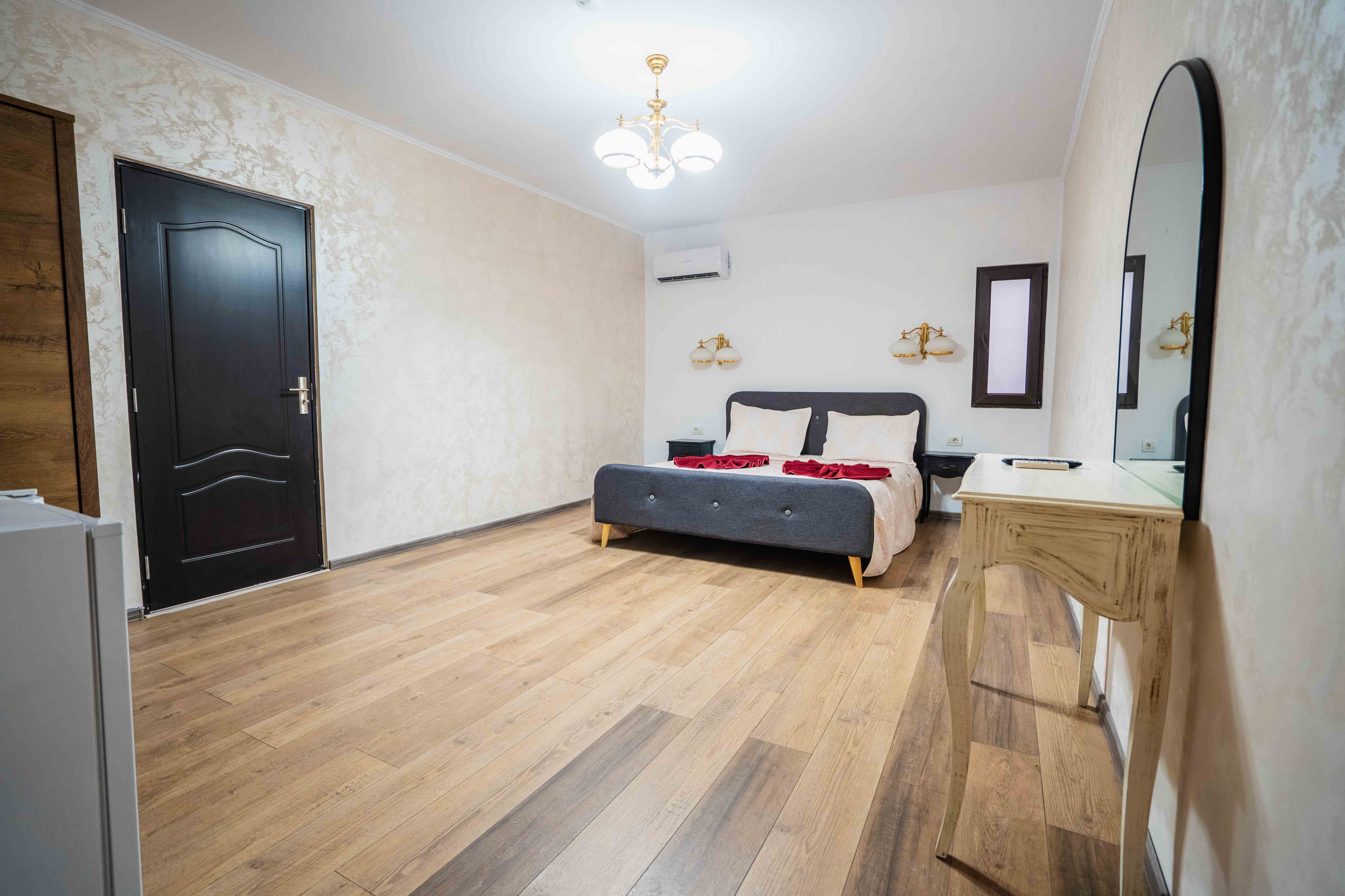 A modern hallway features vibrant teal and orange geometric and leaf patterns, with glossy tiled floors, a large rectangular light fixture, and a small shelf holding a potted plant, all leading to a large, frosted window at the end.