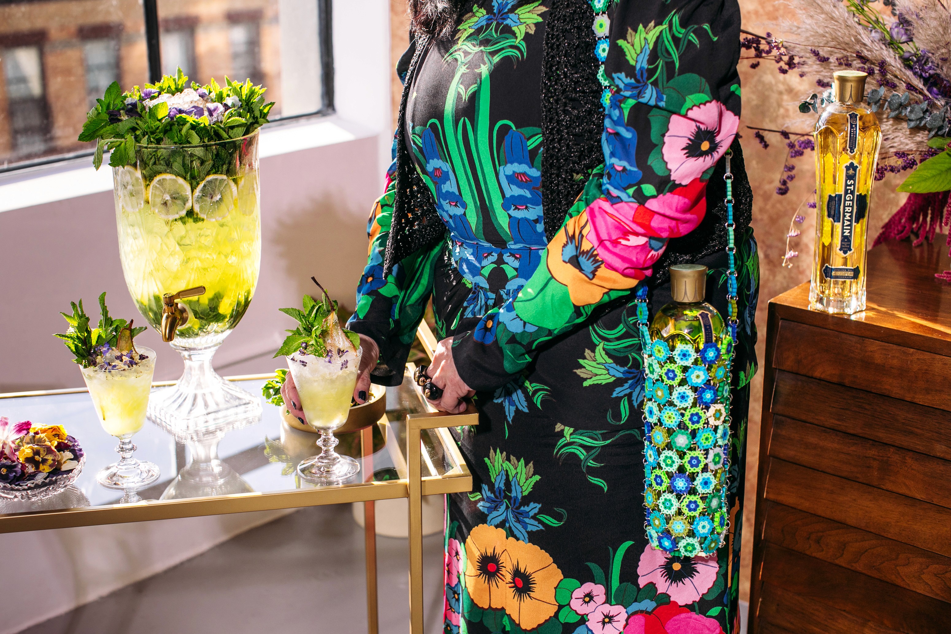 Anna Sui beside a St-Germain punch bowl, cocktails, and floral bottle tote