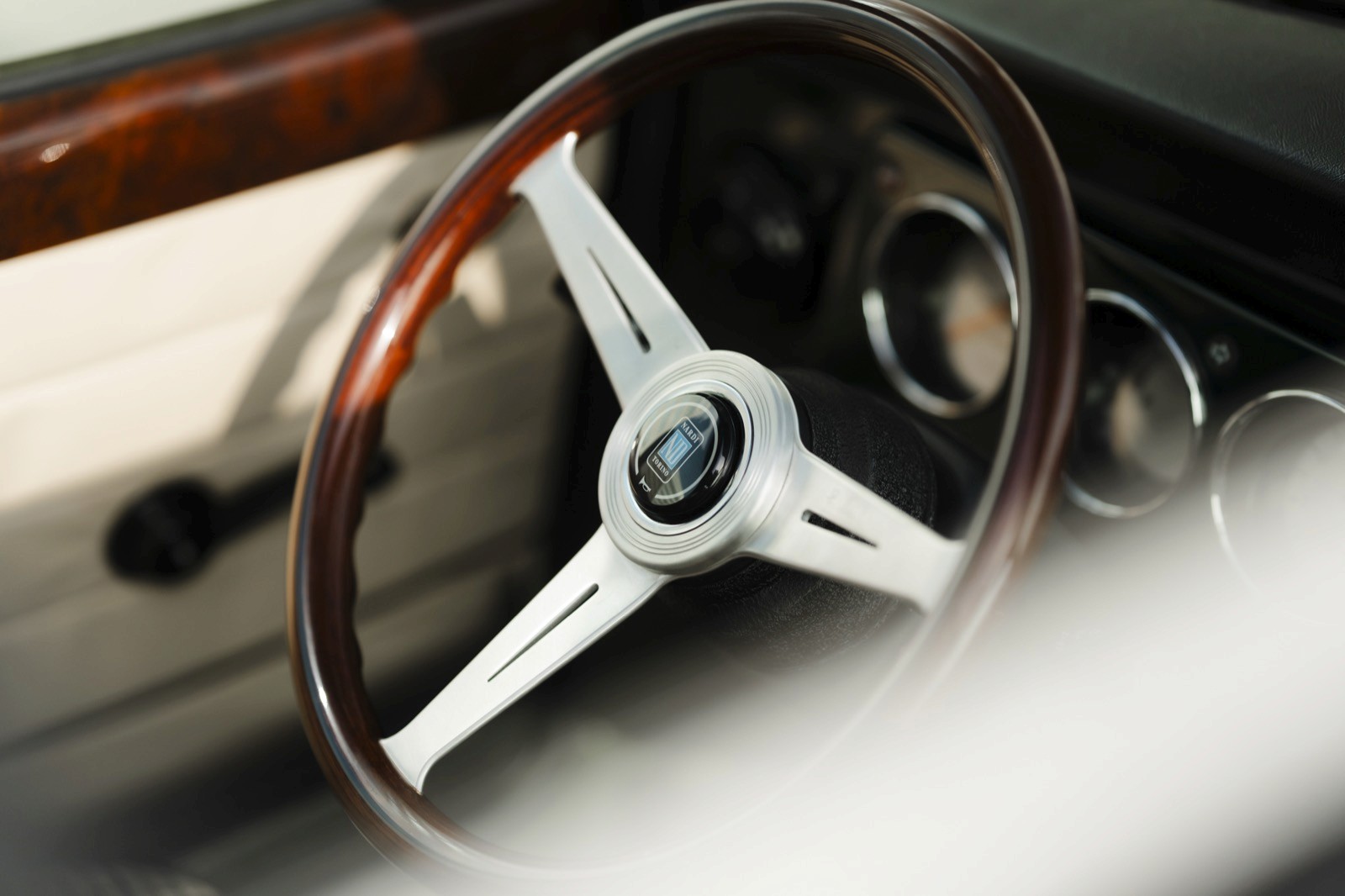 Close-up of a car's steering wheel with a wooden finish and silver spokes, showcasing classic automotive design.