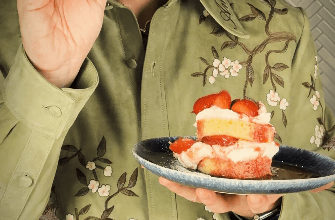 Individually plated layered strawberry shortcake on a blue plate in hand in front of a green embrodered shirt