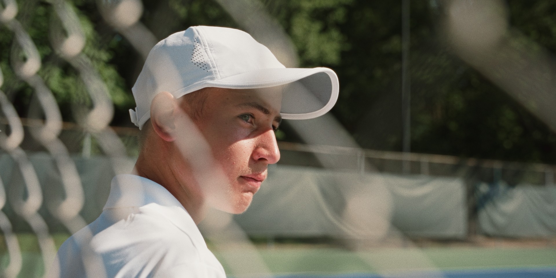 Jeune joueur de tennis concentré au bord du court, casquette blanche vissée sur la tête.