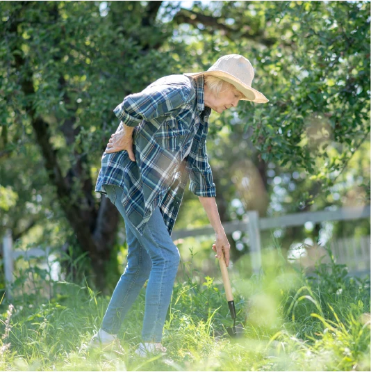 Elderly woman in a garden, bending over in pain while tending plants