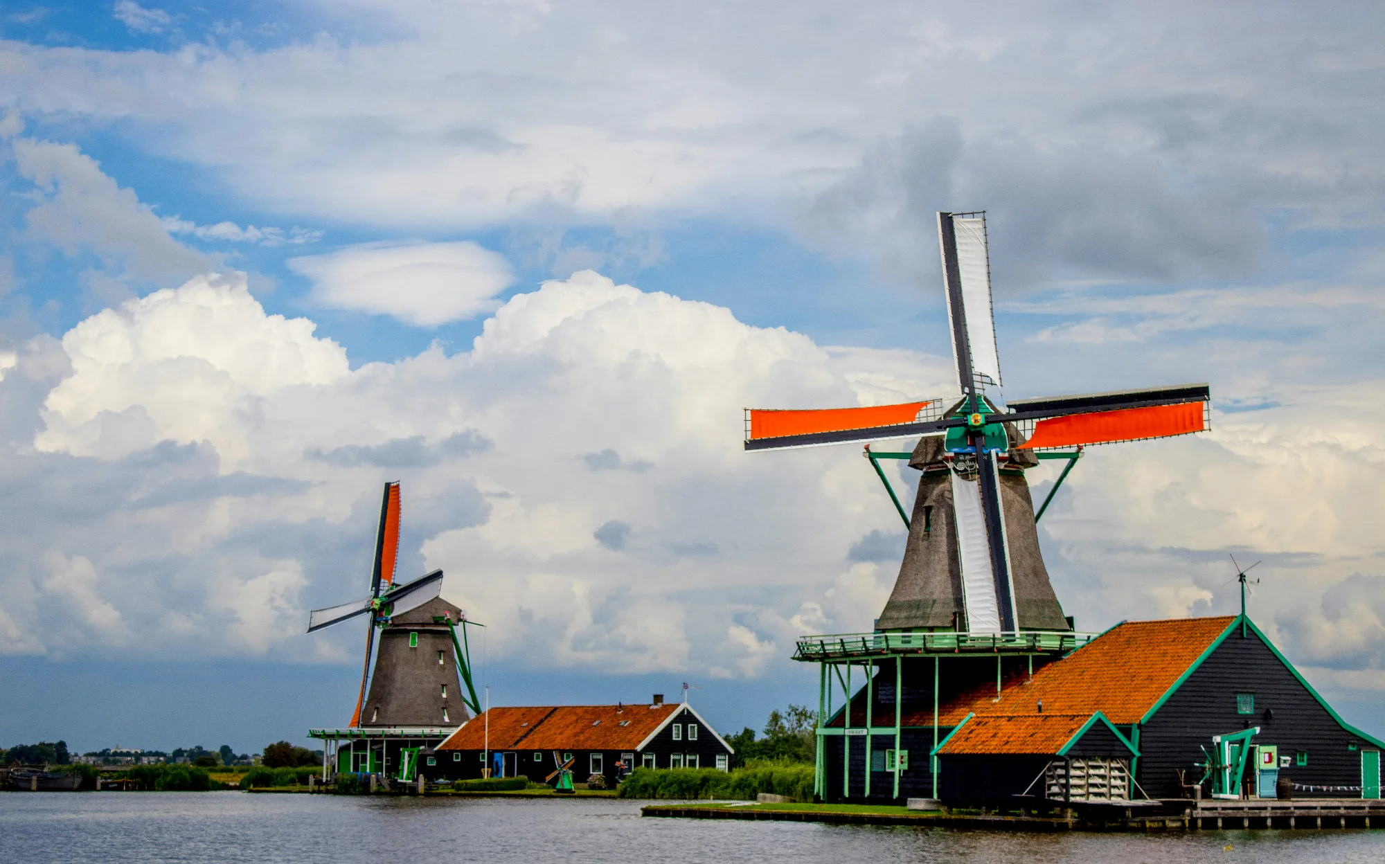 Traditional Dutch windmills with orange and white sails by a canal under a cloudy sky.