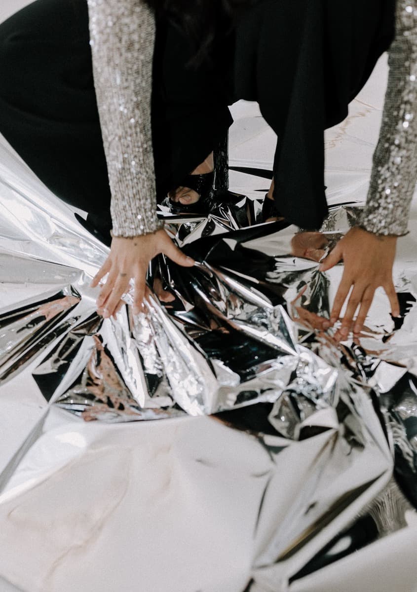 A model kneeling on reflective mylar in a sequined top, evoking a futuristic aesthetic during a creative shoot at Revelator Studio, a Shreveport natural light studio.