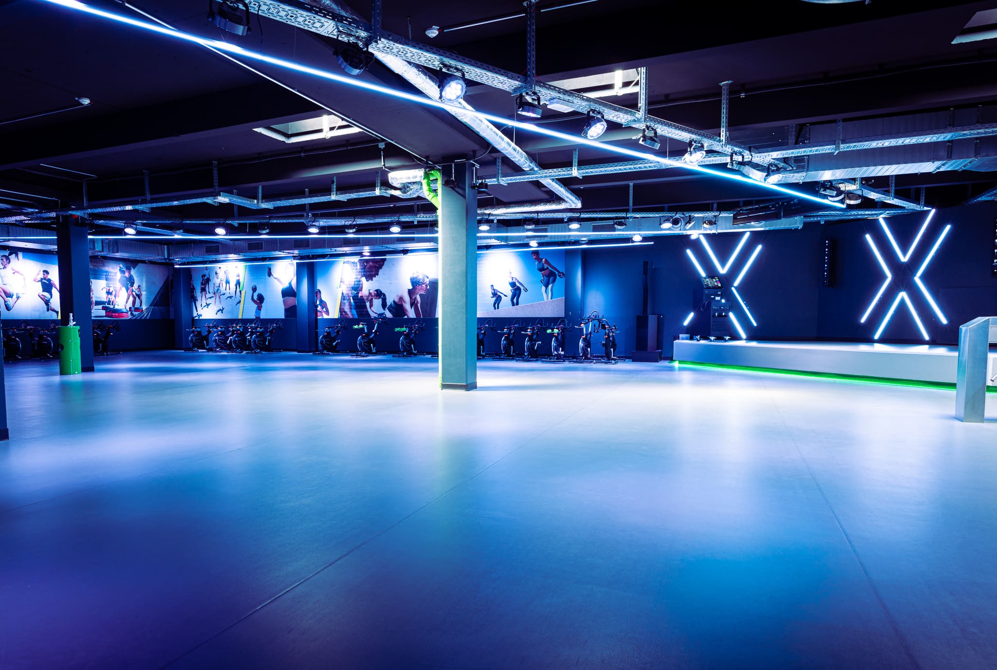  Neonbeleuchteter Kursraum im XTRAFIT Fitnessstudio in Wiesbaden mit hexagonalen Mustern und moderner Bühne.