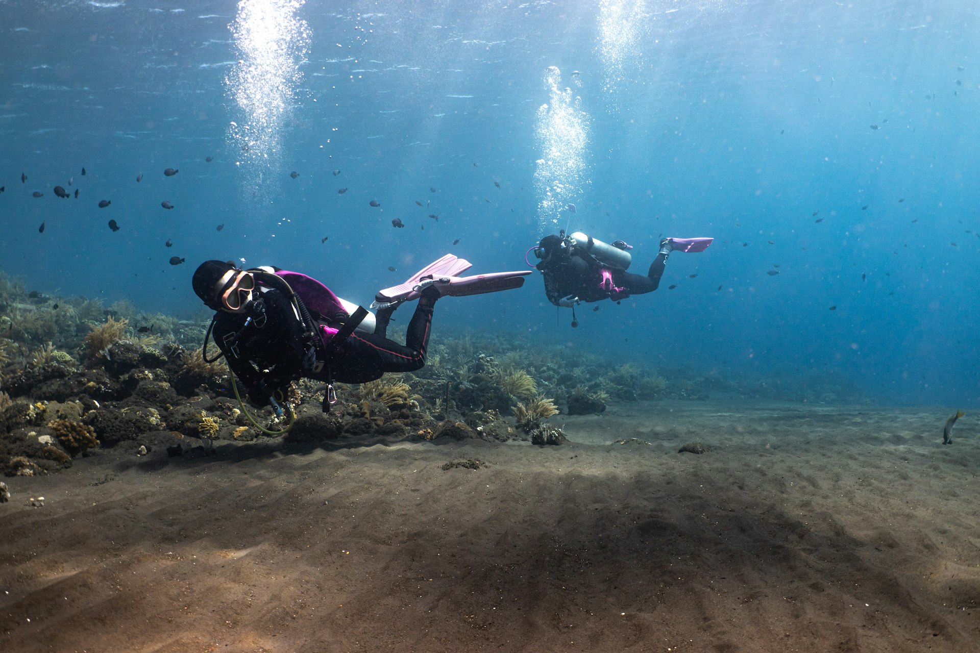 Two scuba divers descending along a sandy seabed on a guided dive in Bali