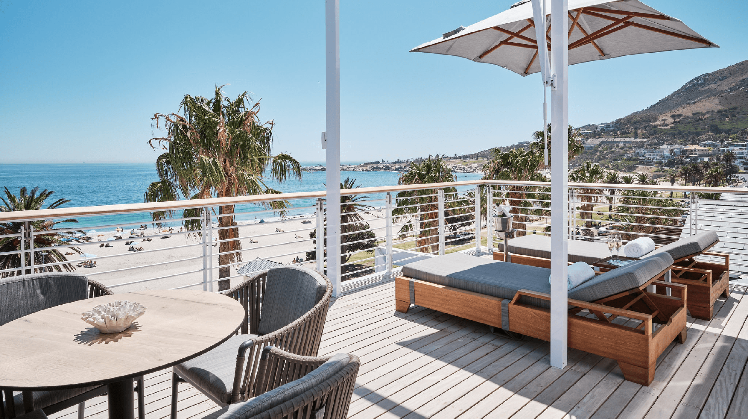 Terrasse mit Meerblick und Liegestühlen. Tisch mit Dekoration und Strand im Hintergrund. Sonnenschein Urlaub