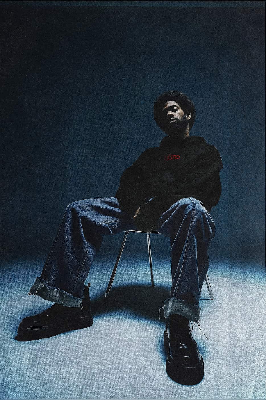 creep red wordmark on black hoodie worn by model sat on chair. 