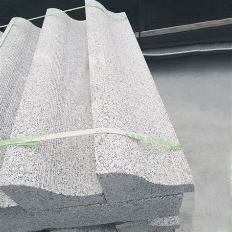 Close-up of textured granite blocks with a wave-like profile, stacked and tied together with green straps. These blocks are ready for transportation or installation in a building project.