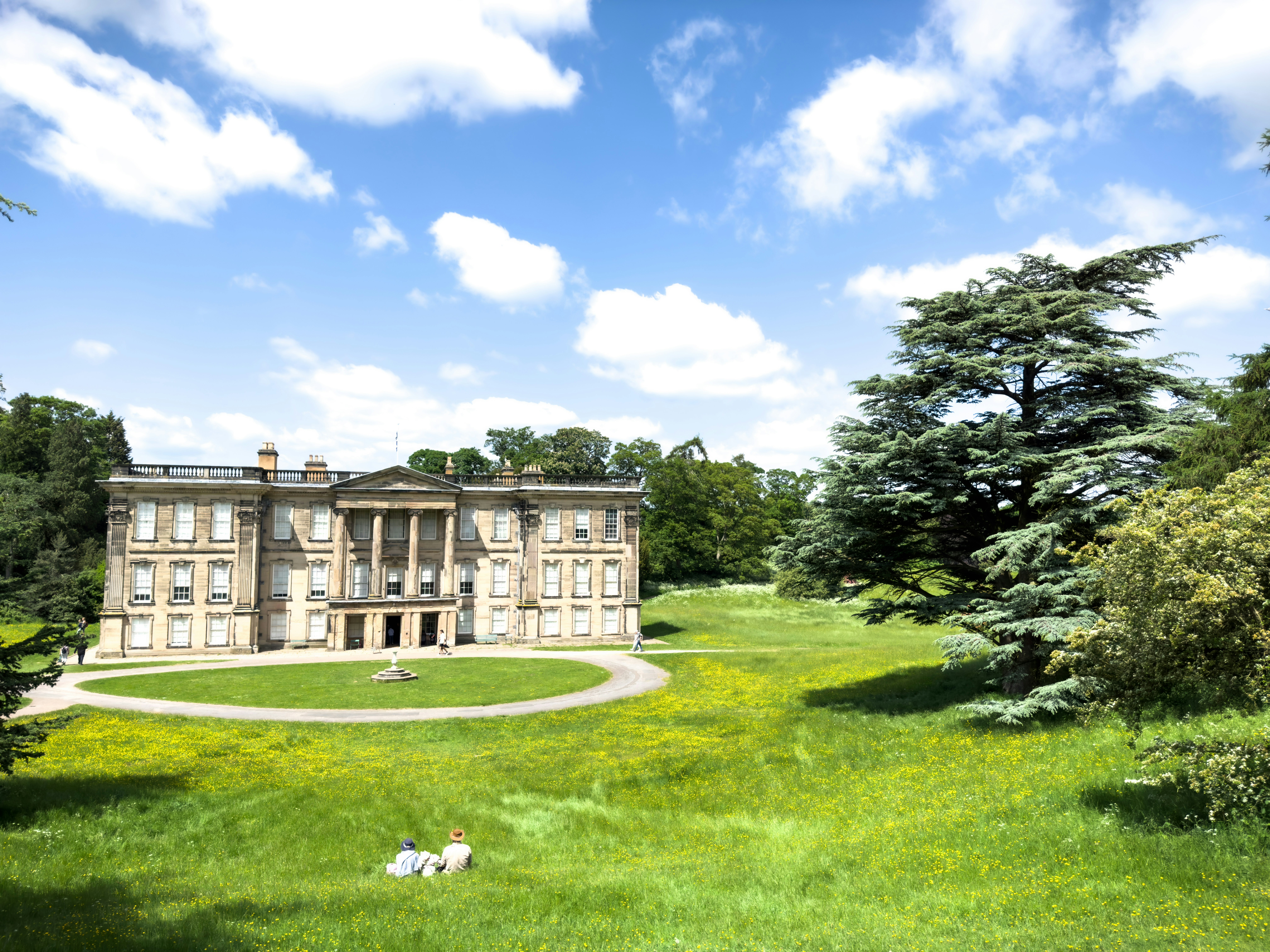 Two people lying on the ground in a royal garden surrounding a traditional-style building.