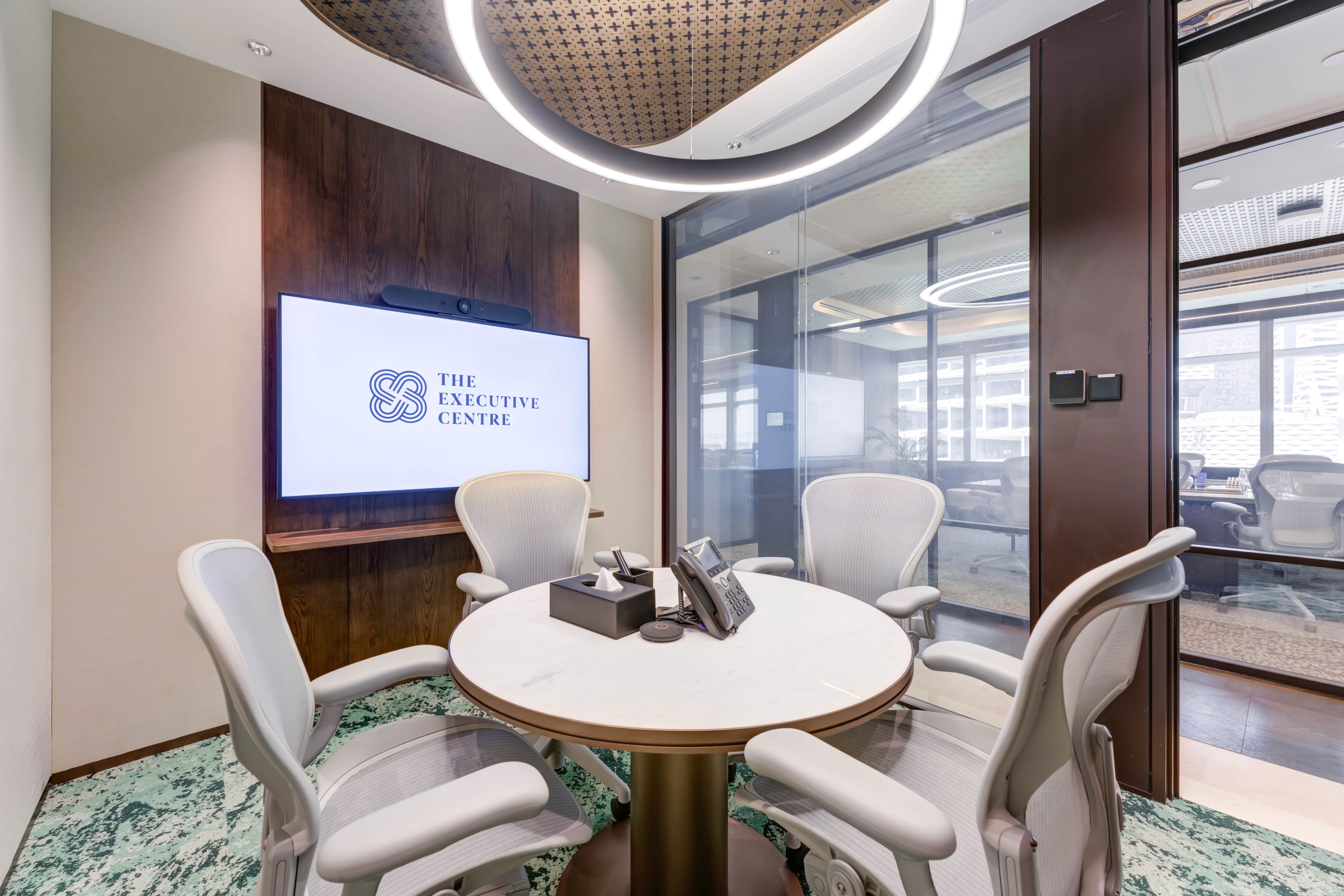 Small round table setup in a modern meeting room with a screen and glass partitions.