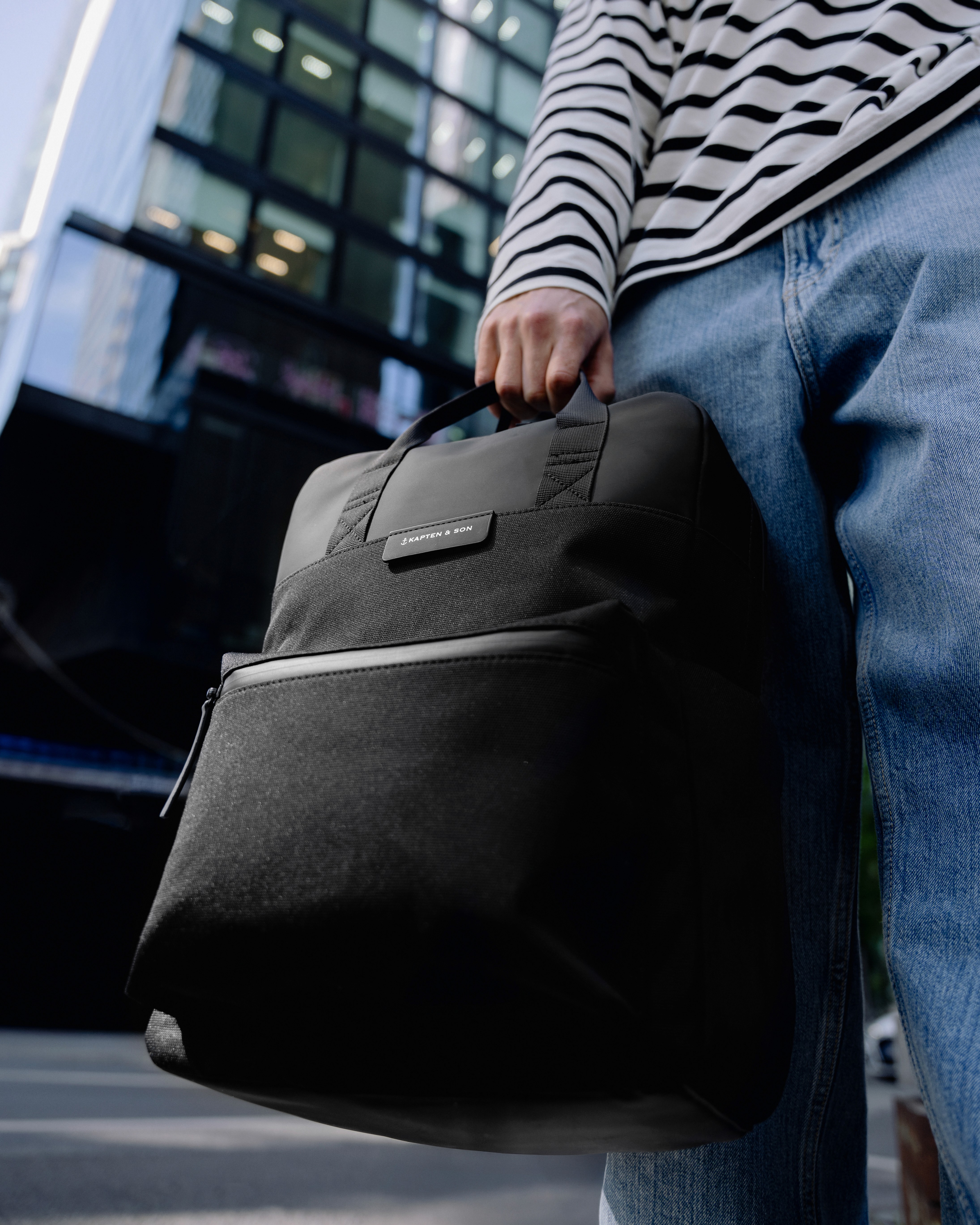 Grosplan d'un sac à dos en nylon noir tenu par une main dans un décor urbain