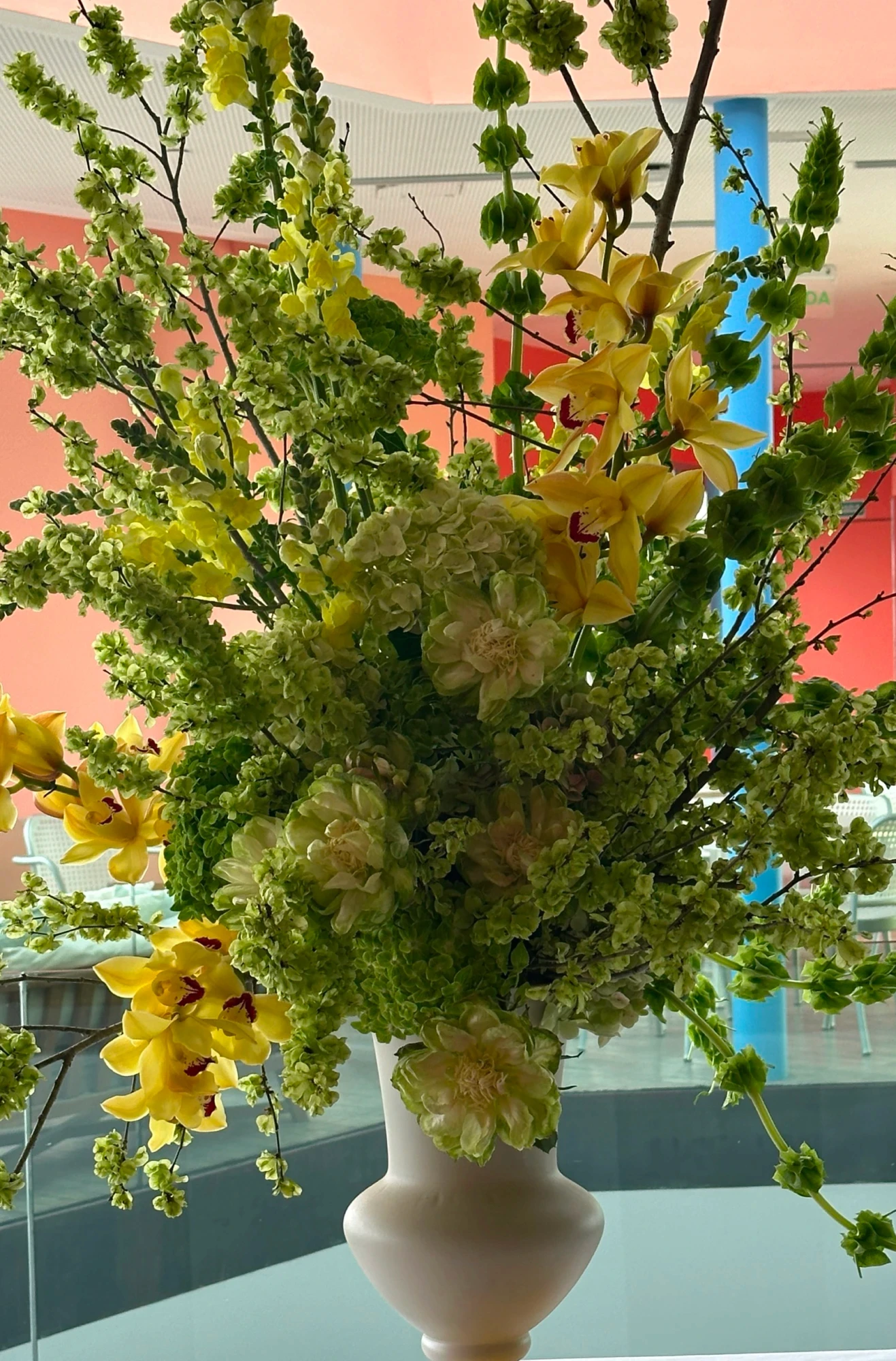 Jarrón blanco con arreglo de campanas de Irlanda verdes, orquídeas amarillas y hortensias en salón moderno.