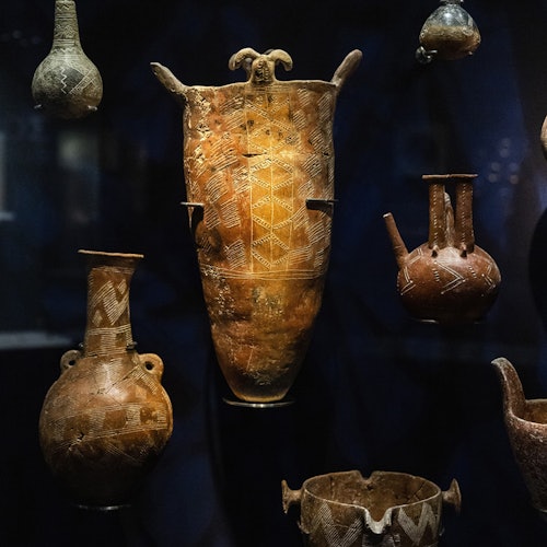 深色背景下展示了多件带有精美纹饰的古代陶器,包括碗、罐和一件高大的器皿。