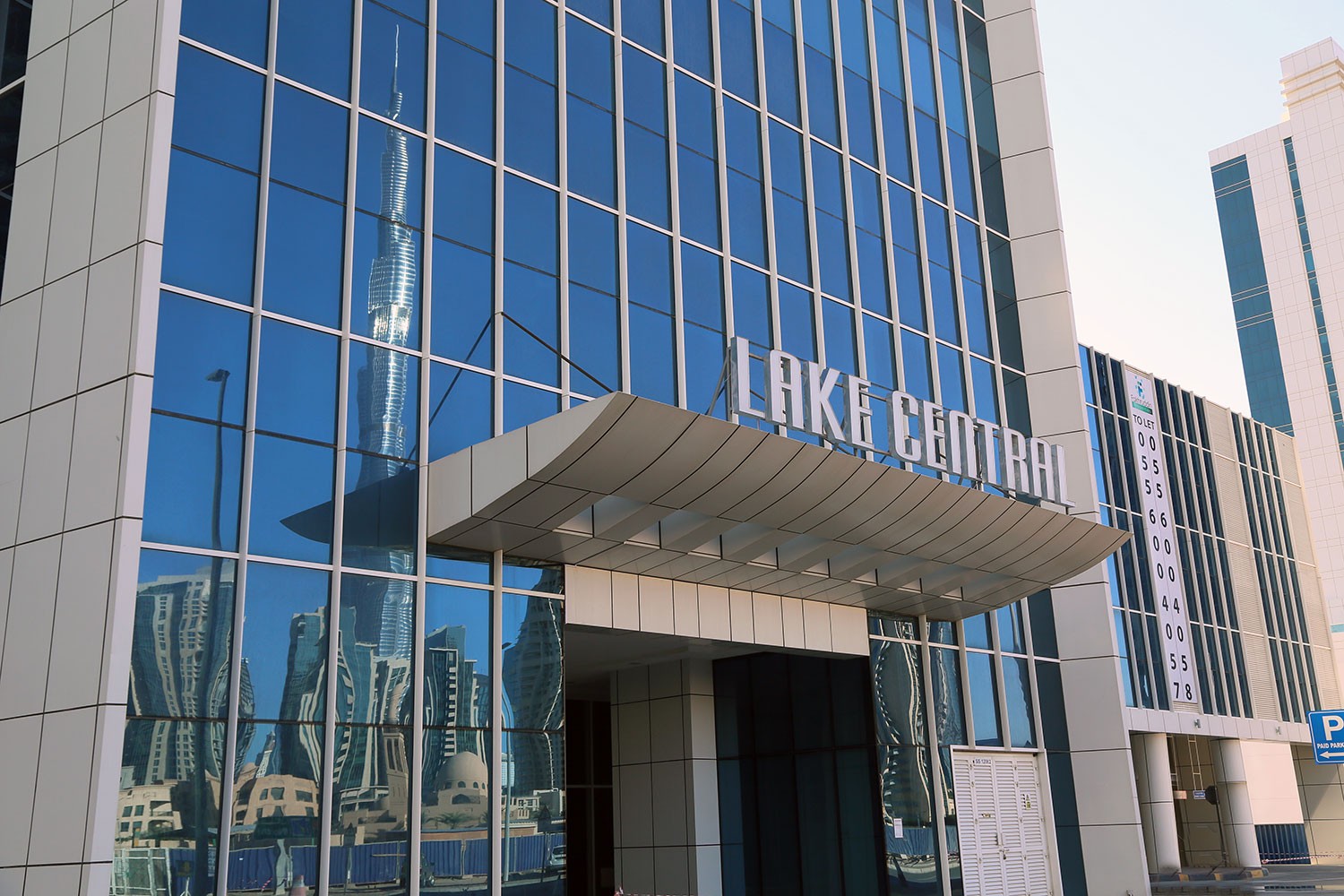 Main entrance of Lake Central with Burj Khalifa's reflection on the polished glass windows.