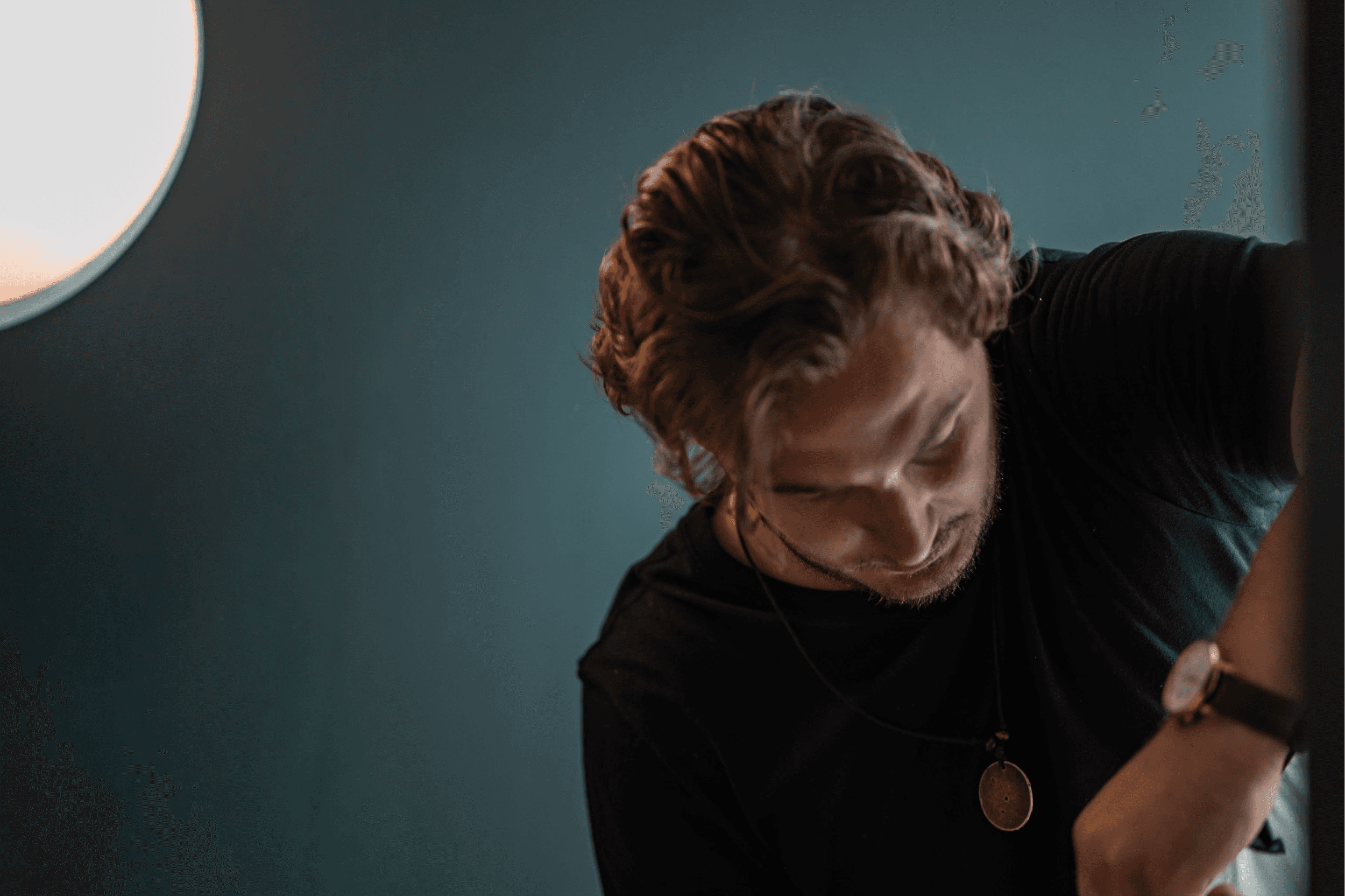 A person sits at a cluttered desk in a dimly lit room, focused on two monitors displaying aerial maps. The walls are covered with various images and notes.