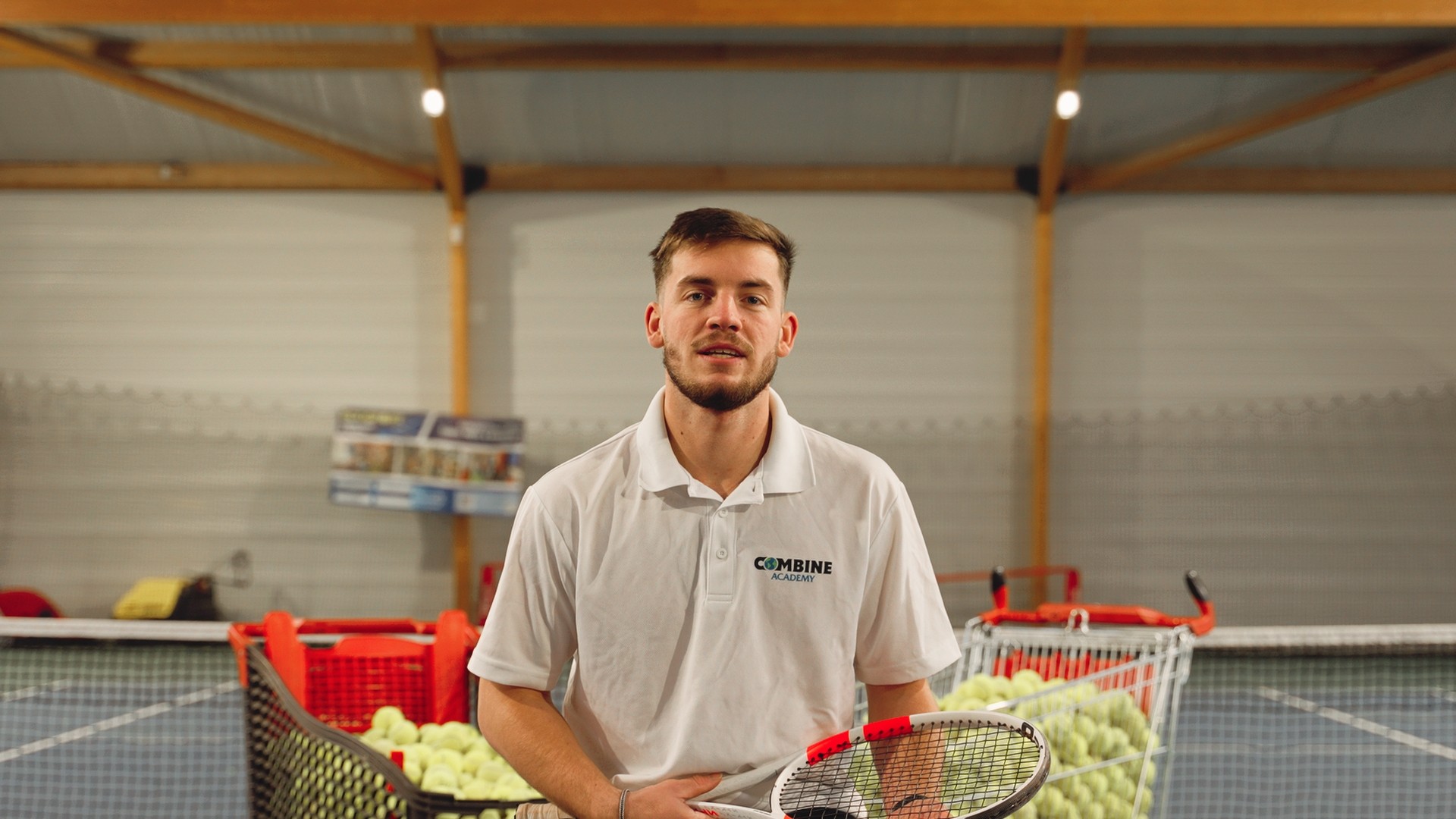 Portrait d’Aurélien Arlot, coach de tennis, devant des paniers remplis de balles.