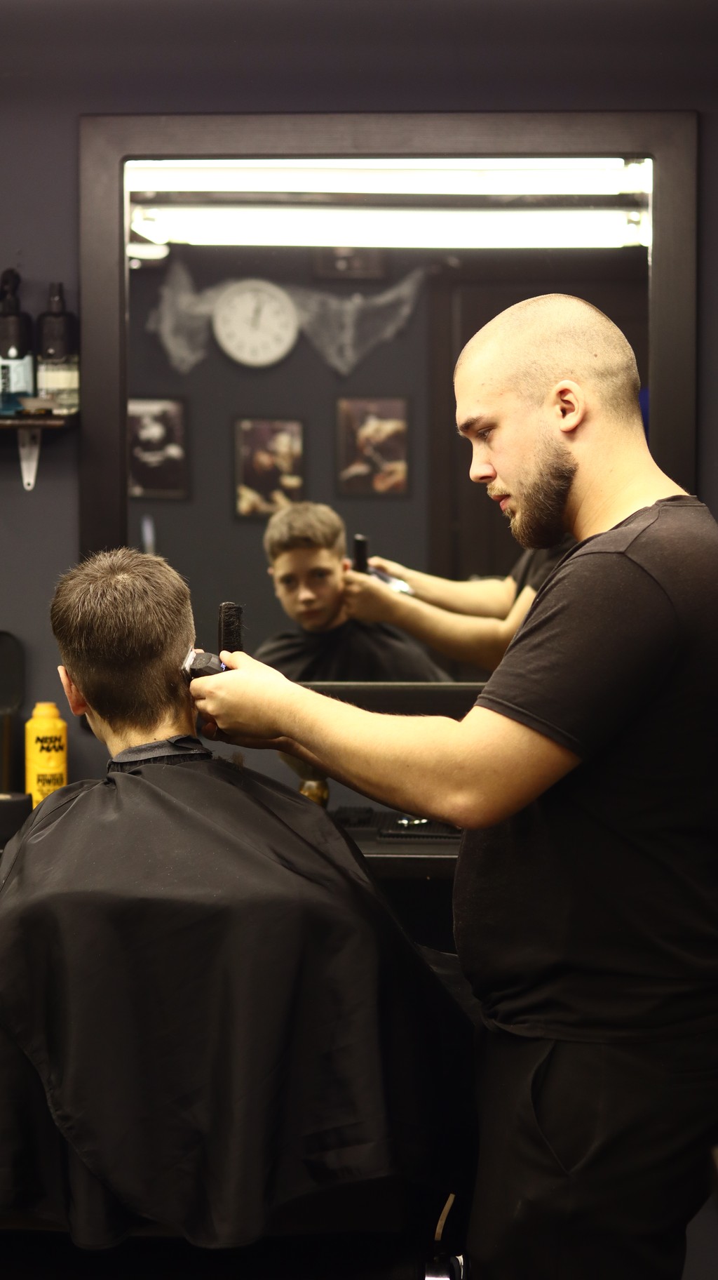 A barber styles a client's hair in a well-lit salon, focused on creating a precise look.