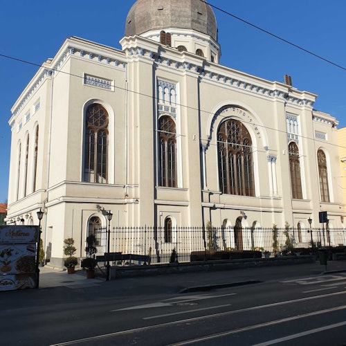 一座大型白色建築,設有拱形窗戶、圓頂和華麗的外立面,坐落在一條安靜的街道上,藍天萬里無雲。