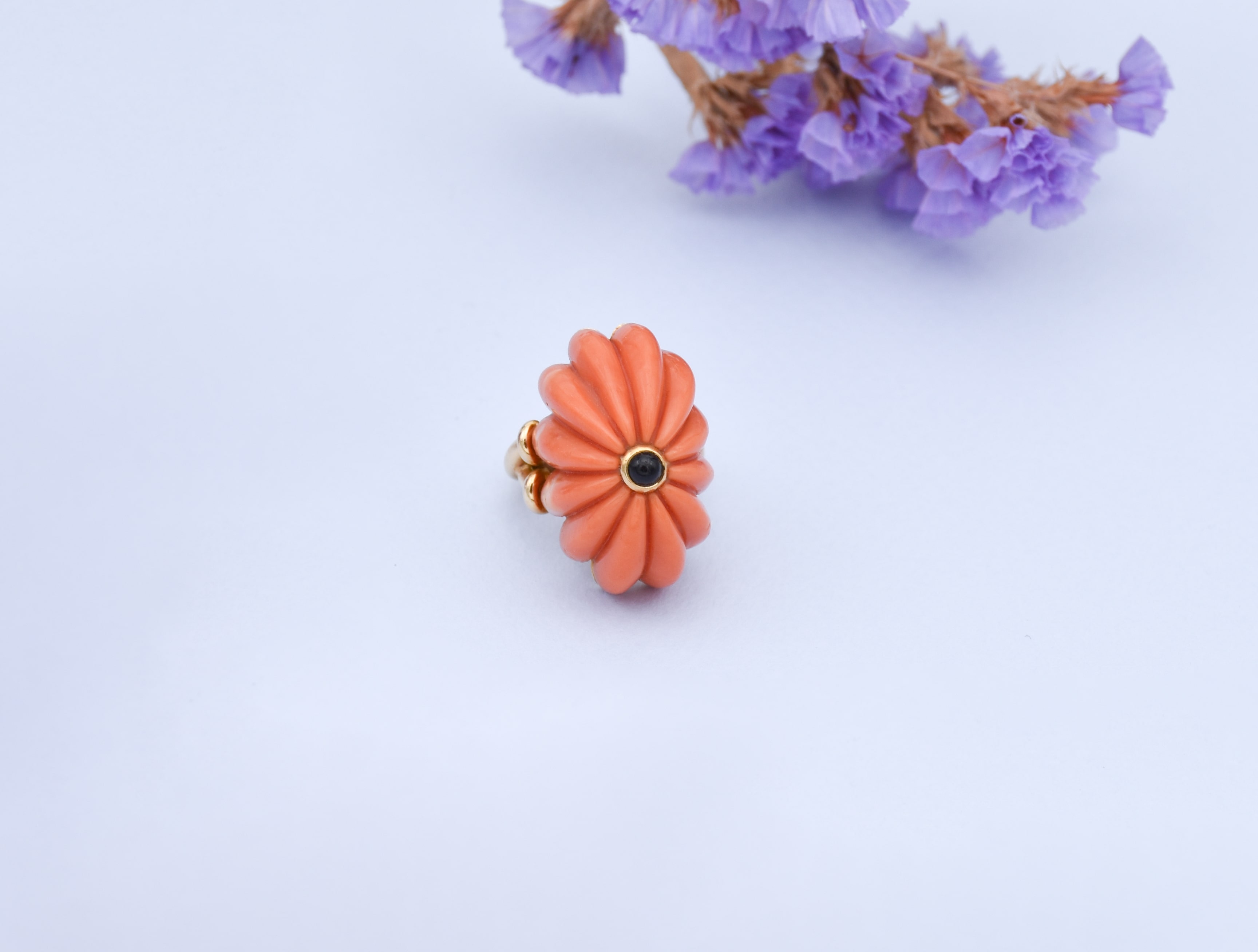 Vue de face d'une bague Chaumet en corail en forme de fleur avec un petit cabochon d'onyx sur le dessus 